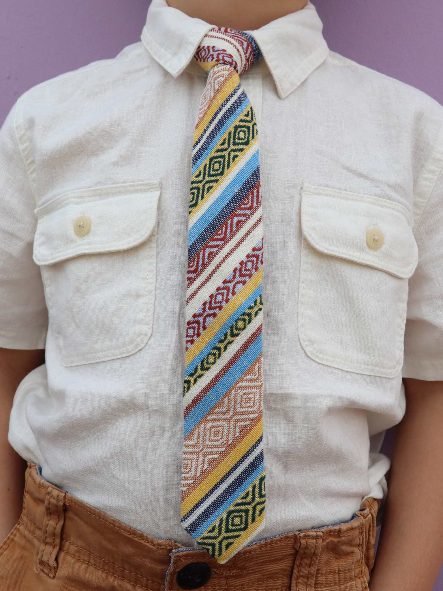 The torso of a boy wearing a striped kids tie with yellow stripes, blue lines, beige bars and Native American designs.