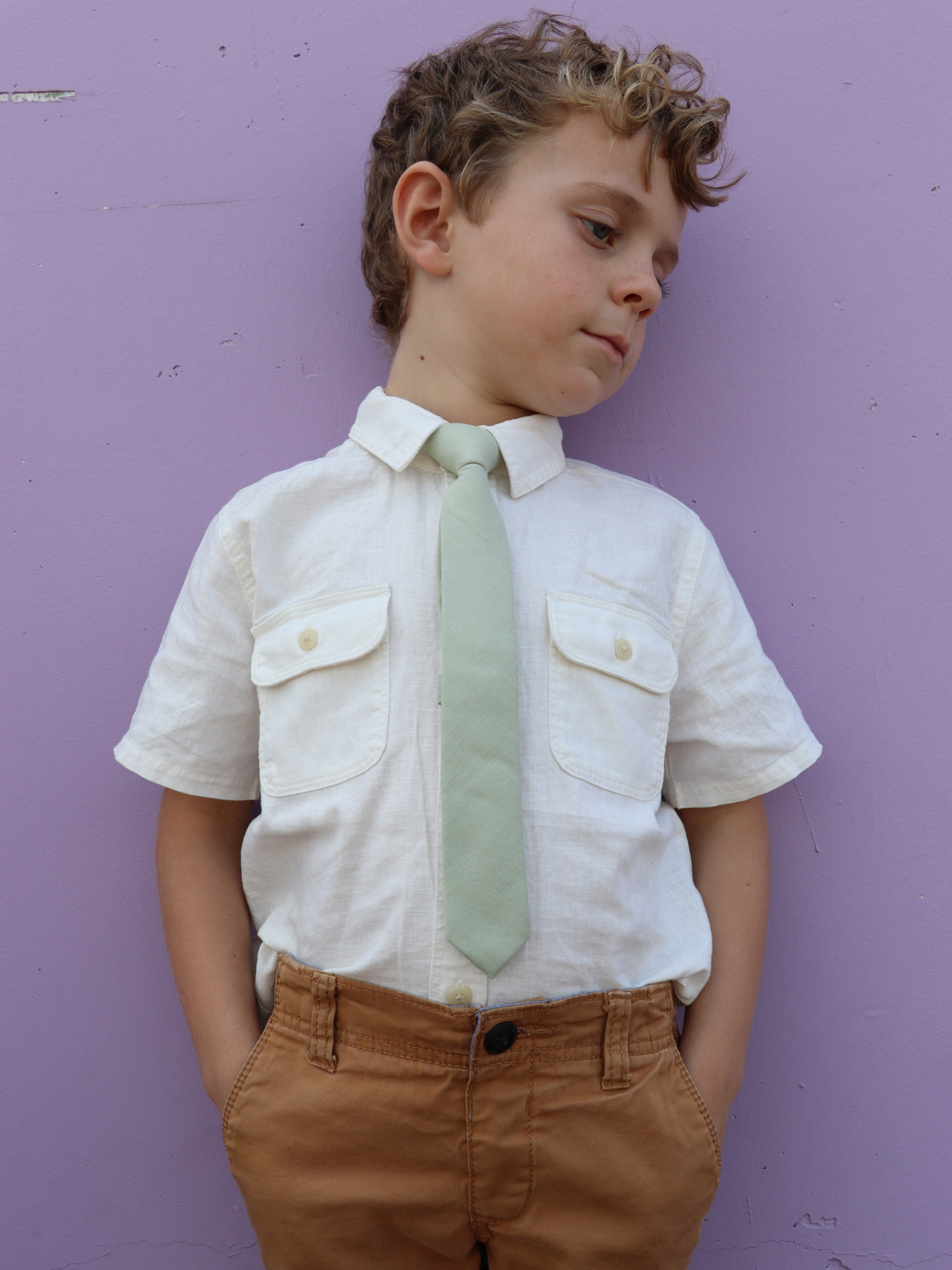 A boy in a white shirt with a sage green solid colored pre tied tie for kids ages 1-12 available in 4 childrens sizes.