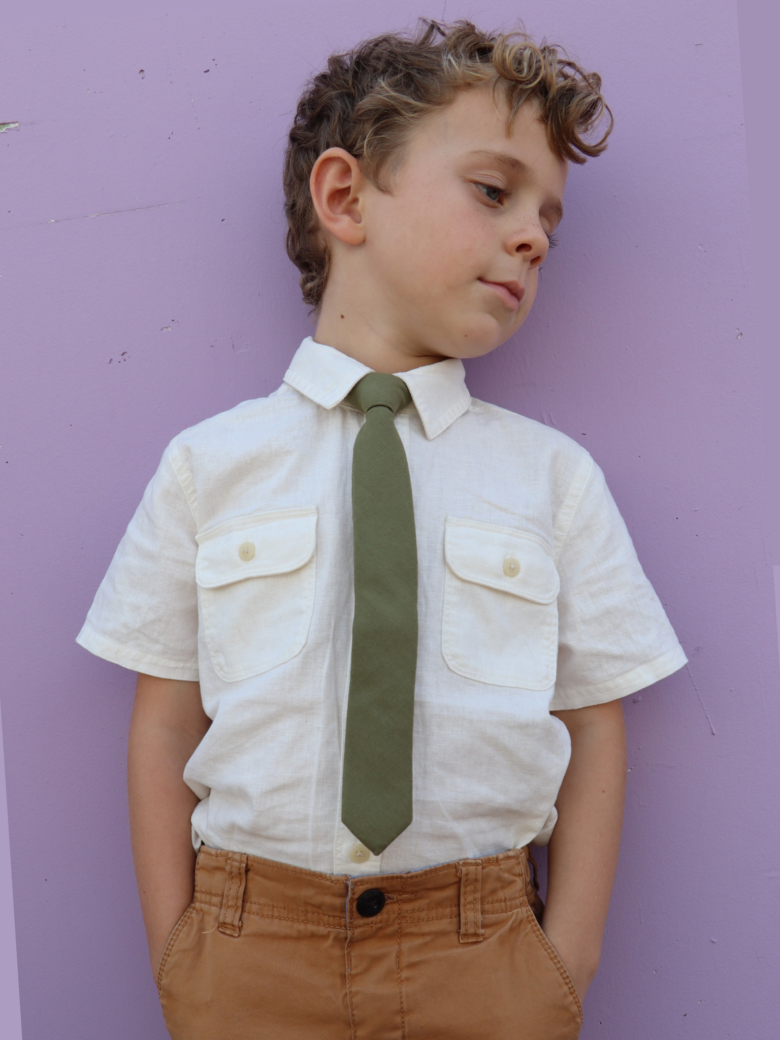 A boy in a white shirt with a military green solid colored pre tied tie for kids ages 1-12 available in 4 childrens sizes.