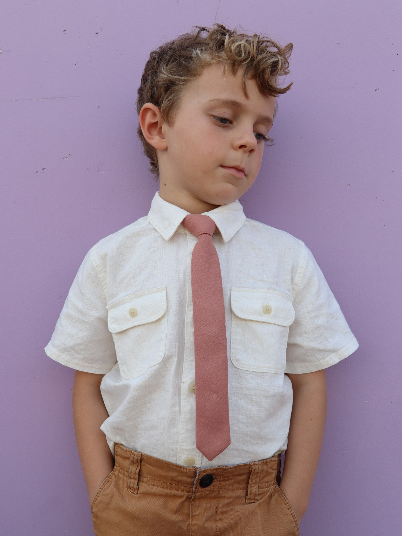 A boy in a white shirt with a rosewood pink solid colored pre tied tie for kids ages 1-12 available in 4 childrens sizes.