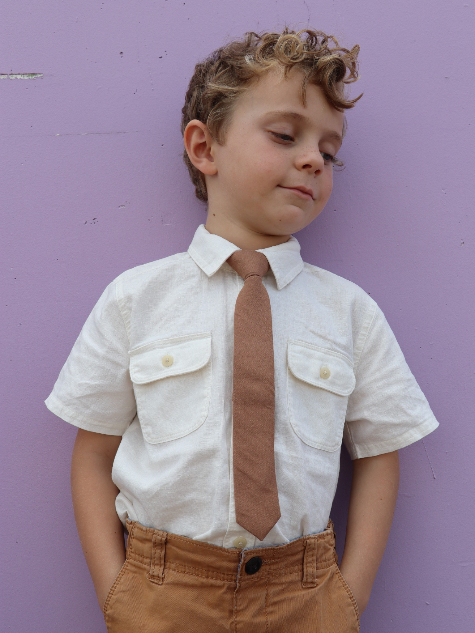 A boy in a white shirt with a light taupe brown solid colored pre tied tie for kids ages 1-12 available in 4 childrens sizes.