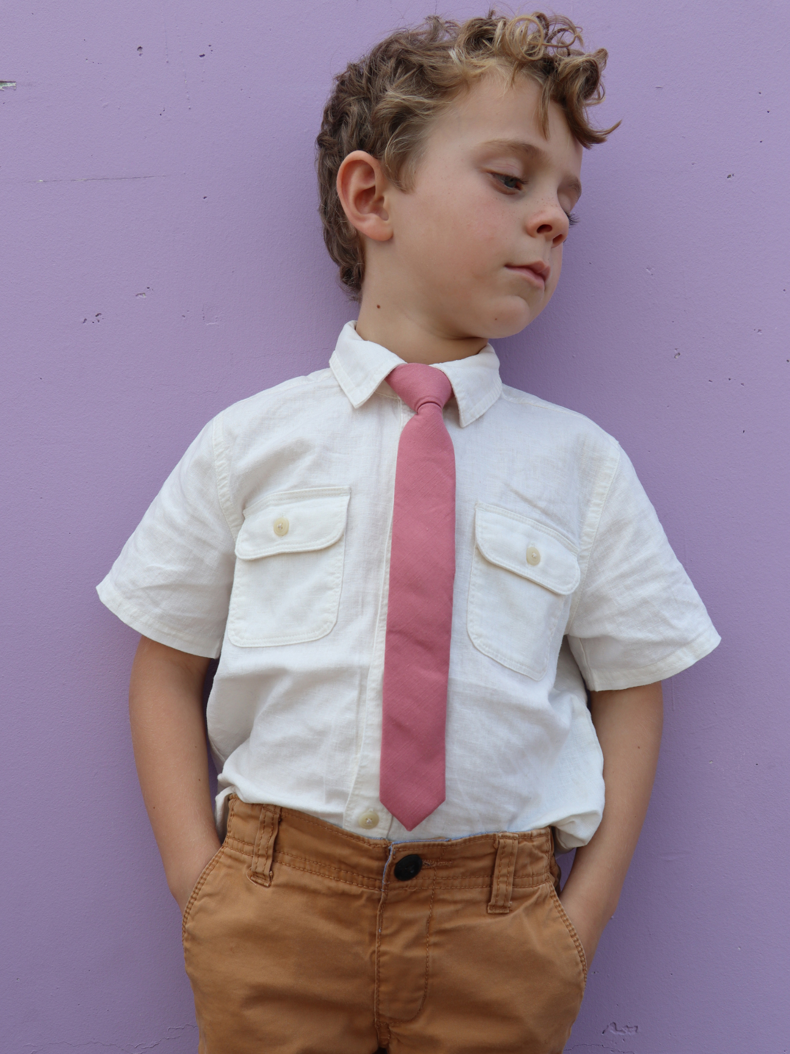 A boy in a white shirt with a rose-gold, pink solid colored pre tied tie for kids ages 1-12 available in 4 childrens sizes.