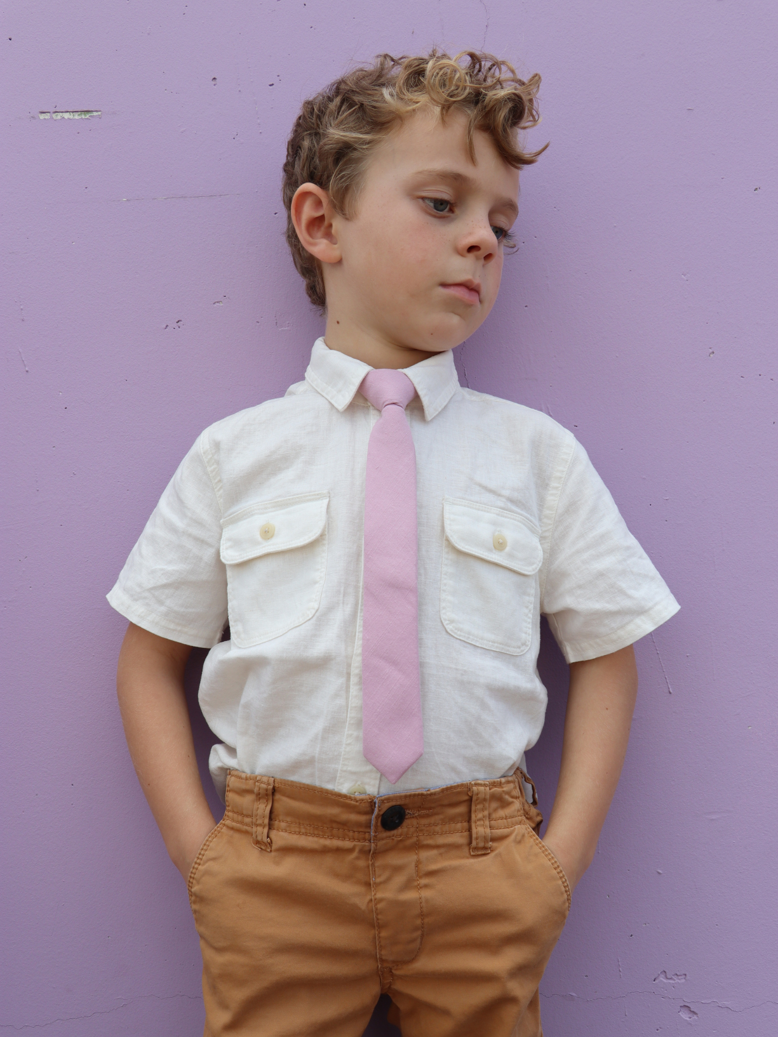 A boy in a white shirt with a dusty rose pink solid colored pre tied tie for kids ages 1-12 available in 4 childrens sizes.