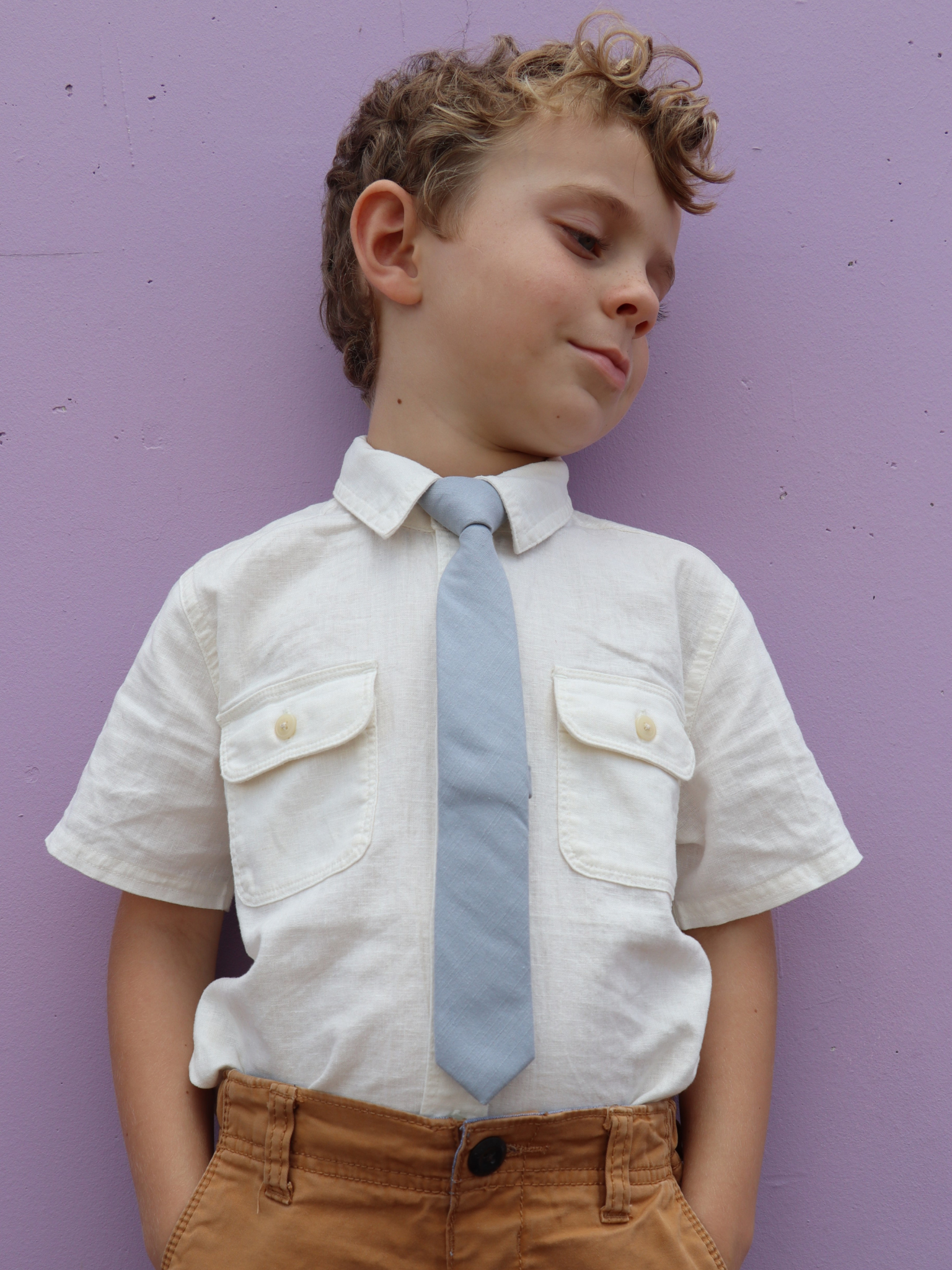 A boy in a white shirt with a pale blue/gray solid colored pre tied tie for kids ages 1-12 available in 4 childrens sizes.