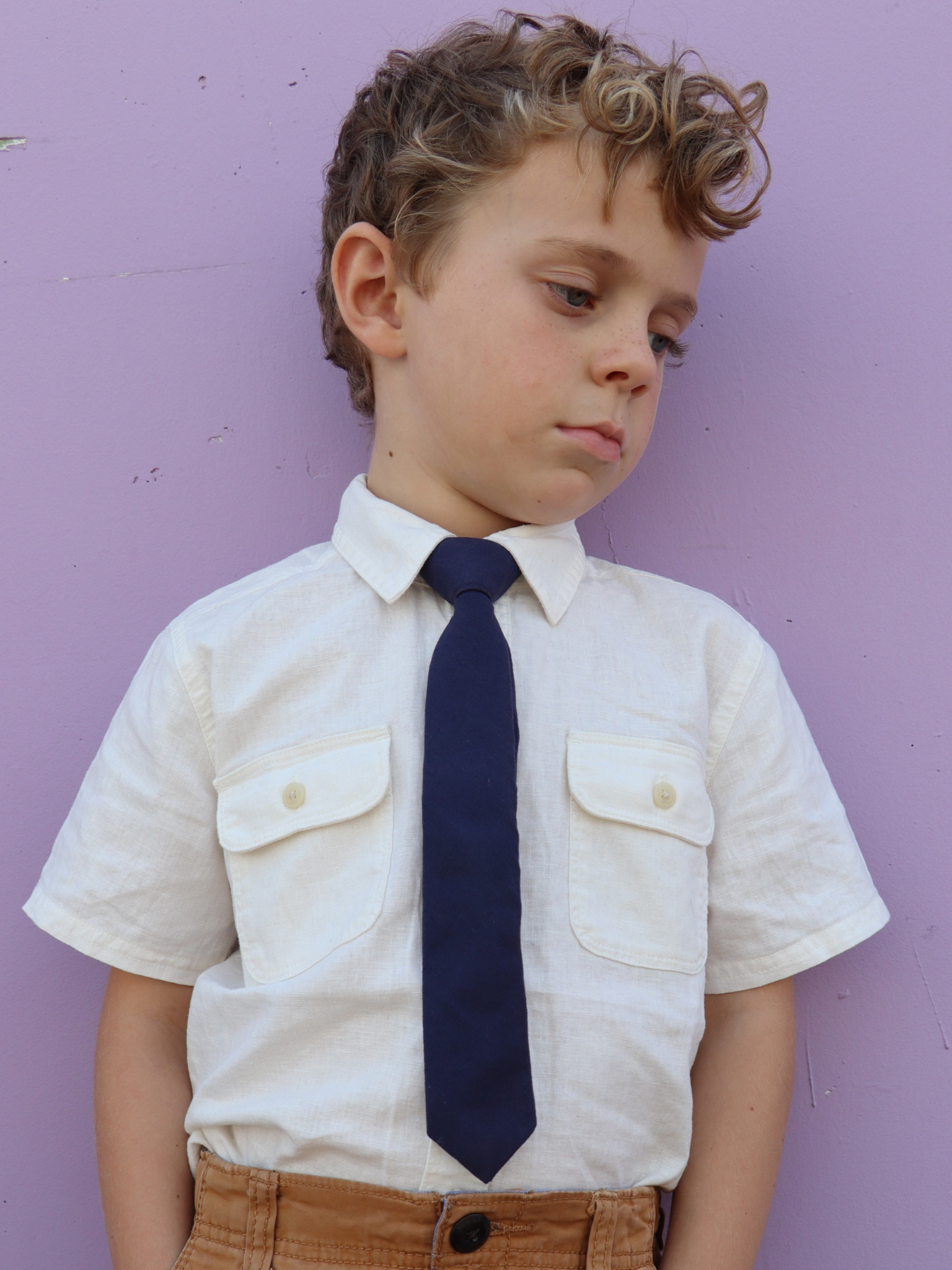 A boy in a white shirt with a navy blue solid colored pre tied tie for kids ages 1-12 available in 4 childrens sizes.