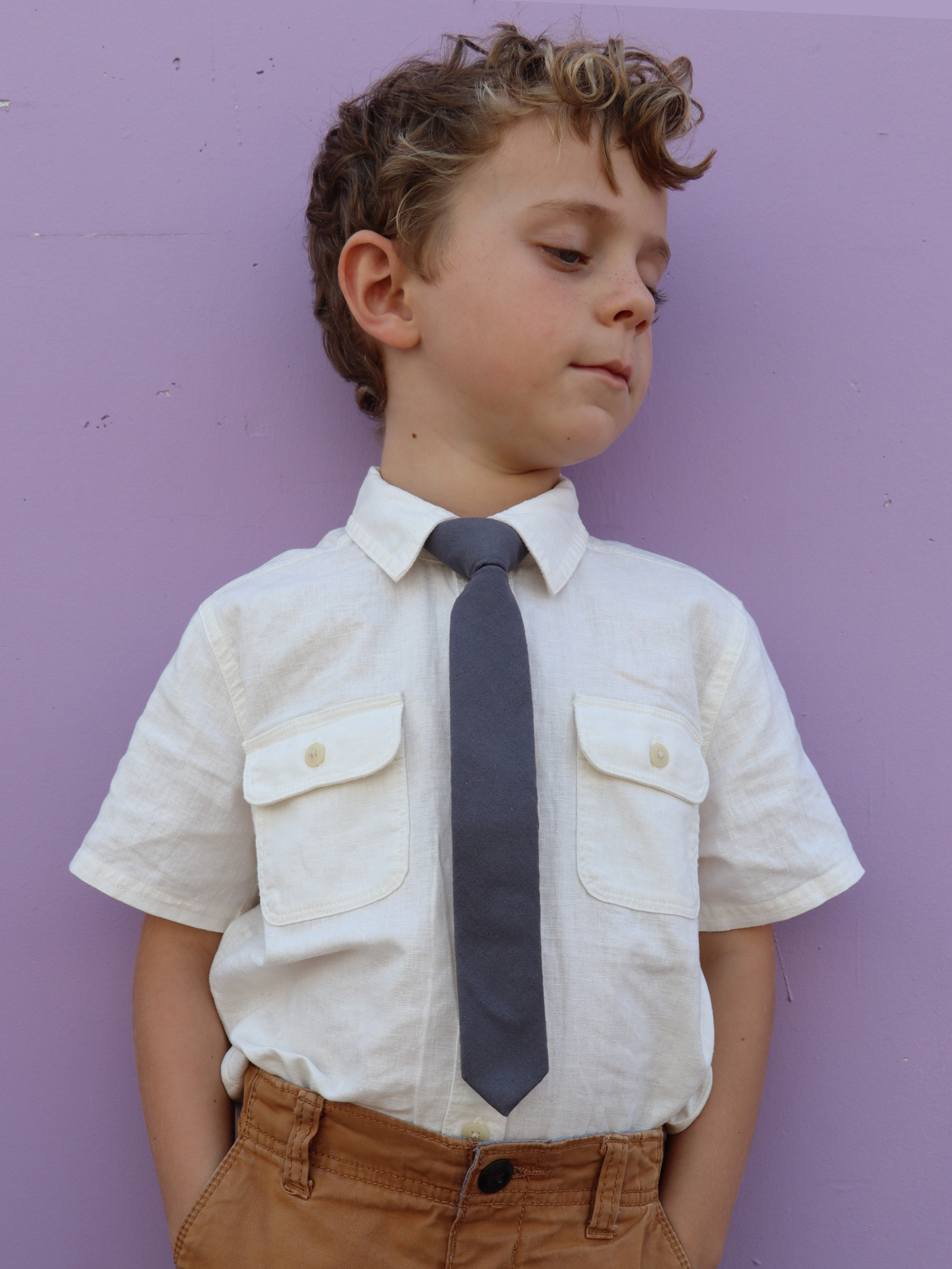 A boy in a white shirt with a dark gray/grey solid colored pre tied tie for kids ages 1-12 available in 4 childrens sizes.