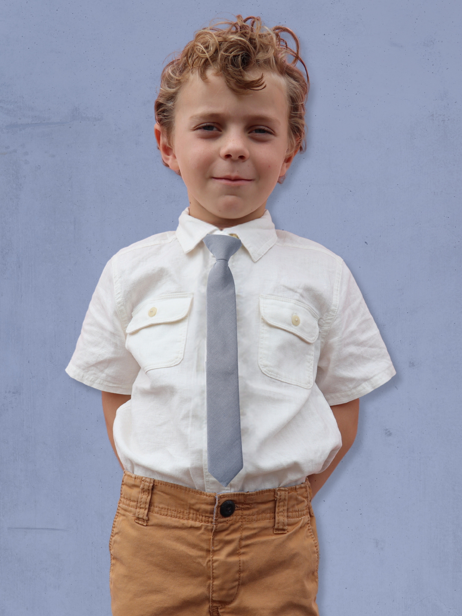 A boy in a white shirt with a light gray-blue solid colored pre tied tie for kids ages 1-12 available in 4 childrens sizes.