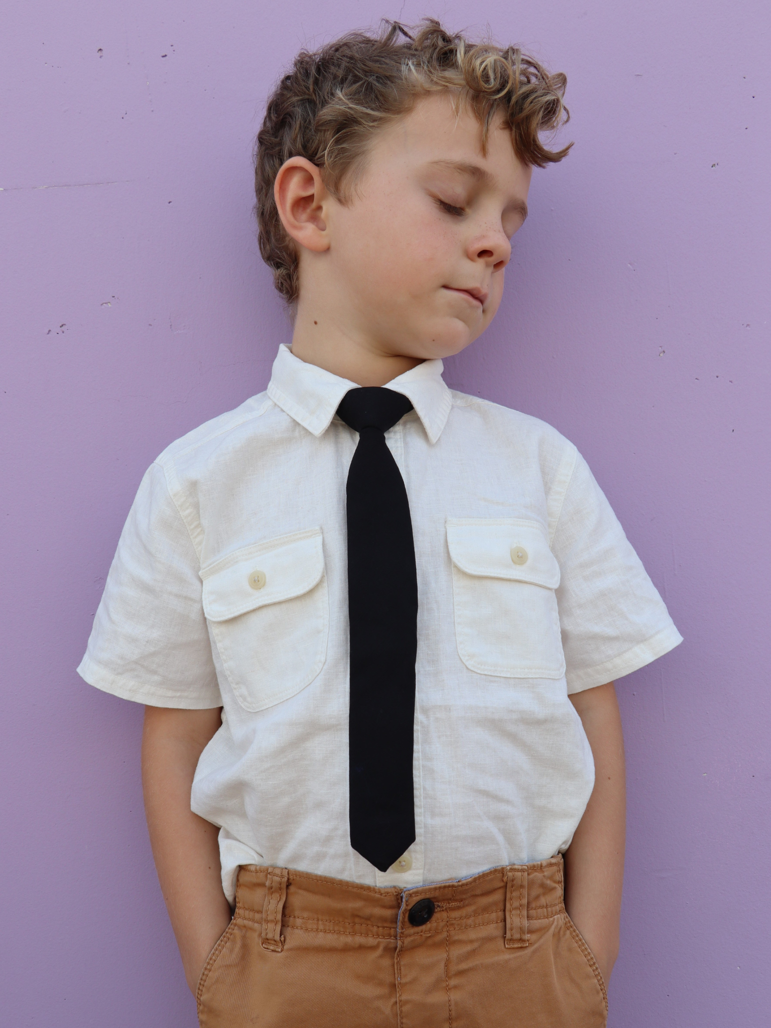 A boy in a white shirt with a pitch black solid colored pre tied tie for kids ages 1-12 available in 4 childrens sizes.