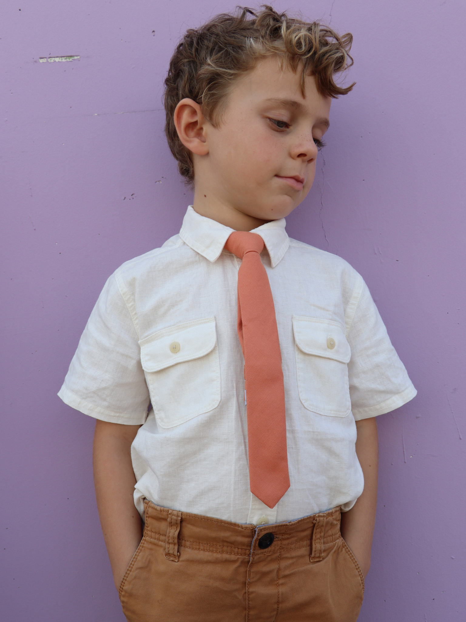 A boy in a white shirt with a burnt orange solid colored pre tied tie for kids ages 1-12 available in 4 childrens sizes.