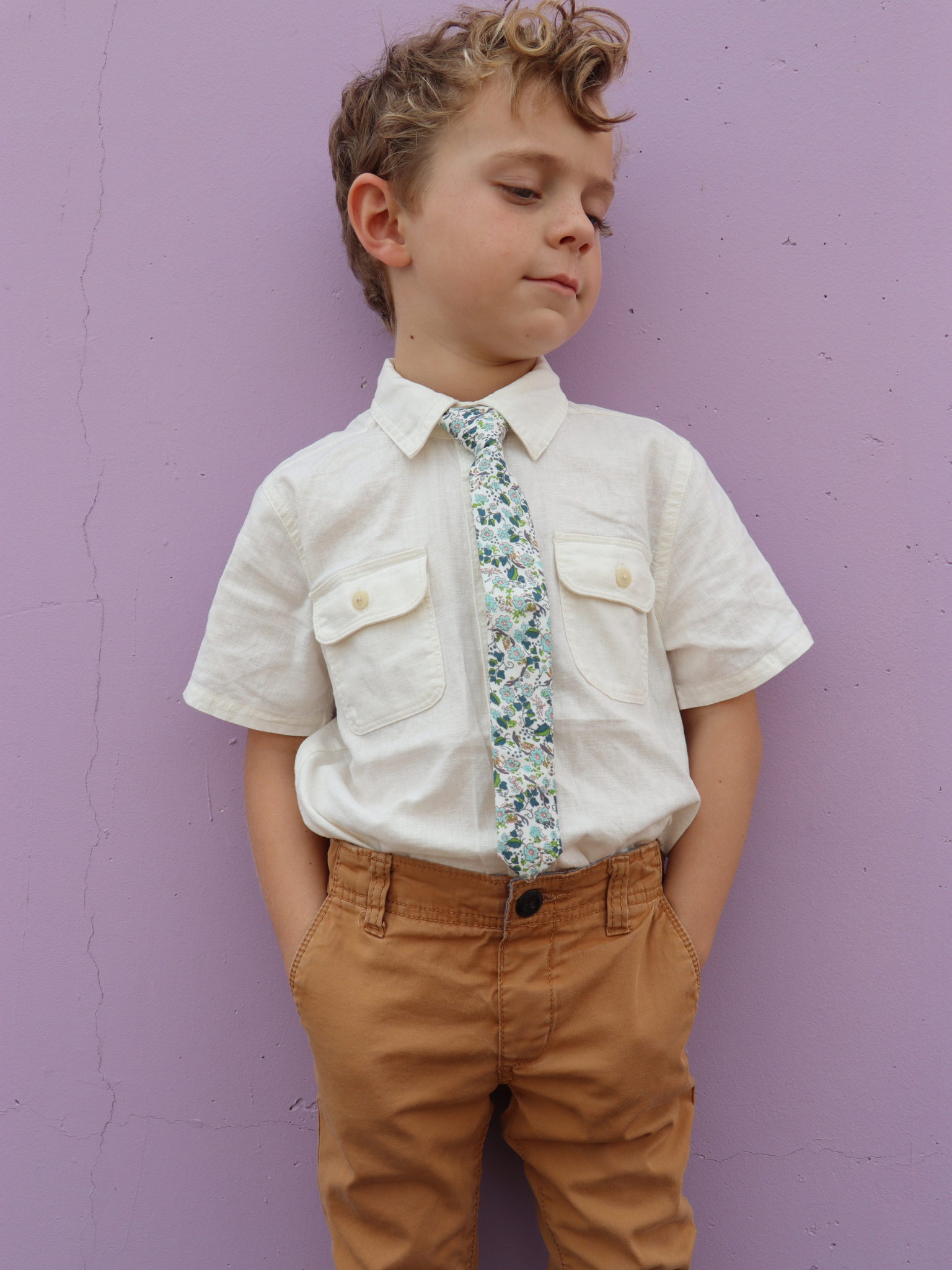 A boy in a white shirt with a white and light blue floral pre tied tie for kids ages 1-12 available in 4 childrens sizes.