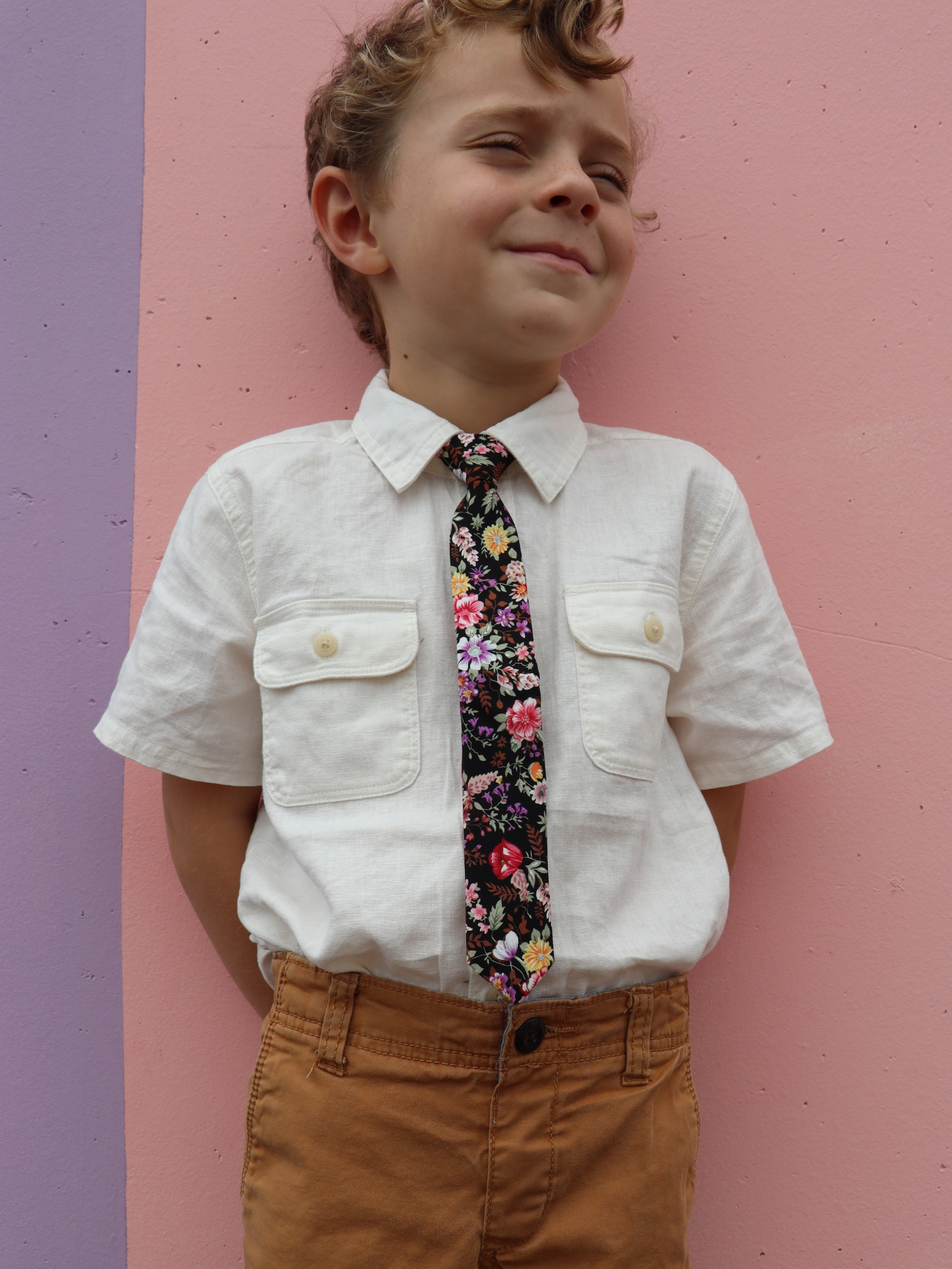 A boy in a white shirt with a black, brown, and pink floral pre tied tie for kids ages 1-12 available in 4 childrens sizes.