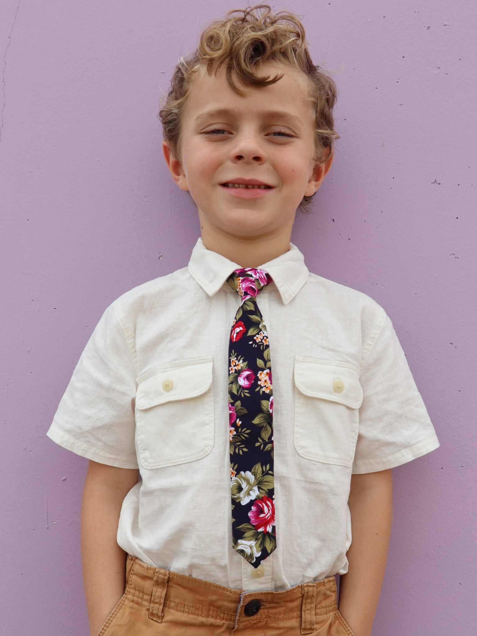 A boy in a white shirt with a navy and pink floral pre tied tie for kids ages 1-12 available in 4 childrens sizes.