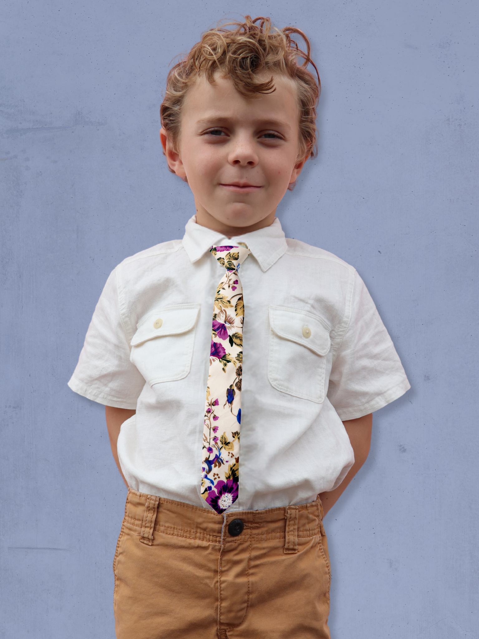 A boy in a white shirt with a beige, blue, and purple floral pre tied tie for kids ages 1-12 available in 4 childrens sizes.