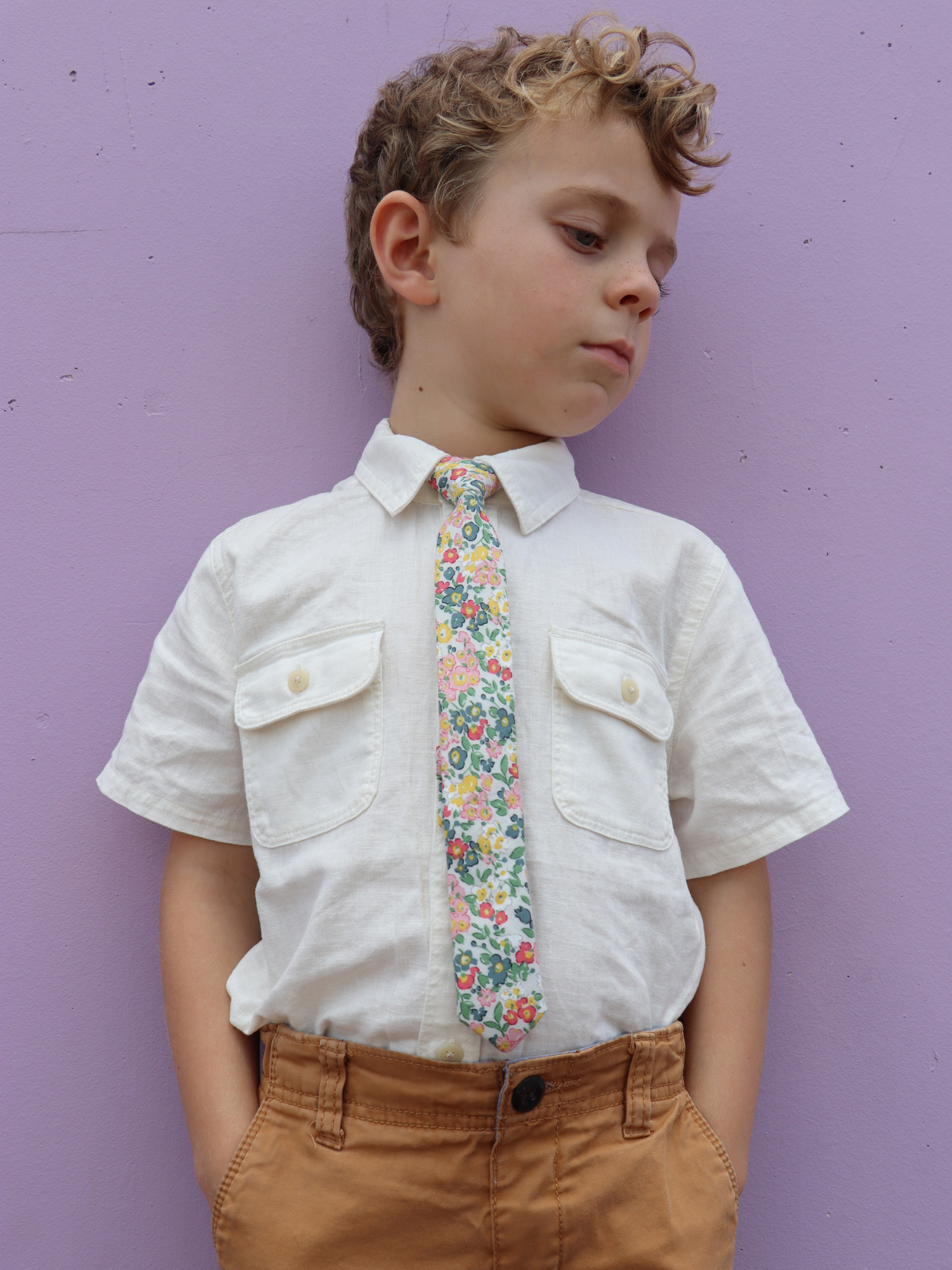 A boy in a white shirt with a white and pink floral pre tied tie for kids ages 1-12 available in 4 childrens sizes.