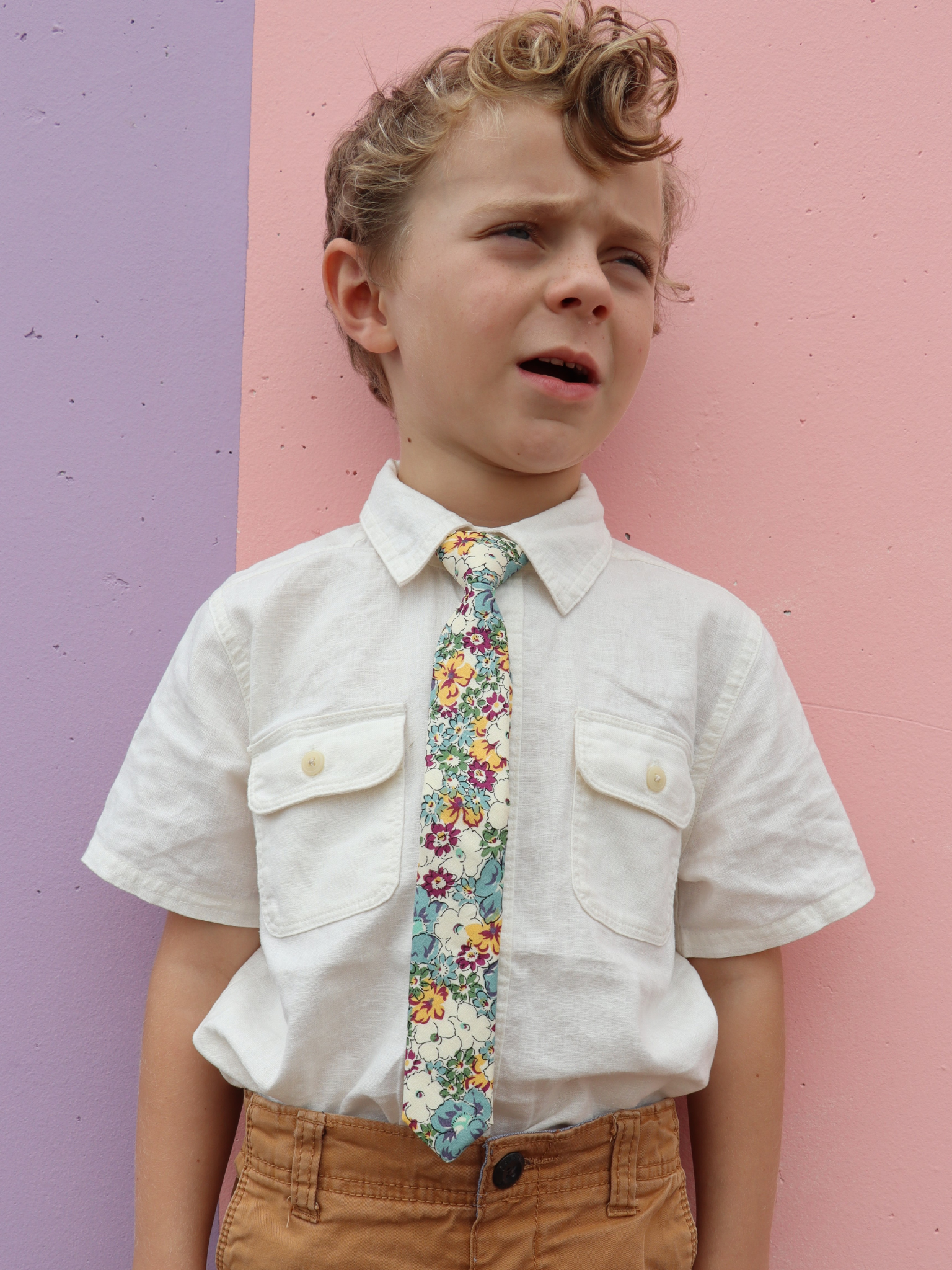 A boy in a white shirt with a white, purple, and blue floral pre tied tie for kids ages 1-12 available in 4 childrens sizes.