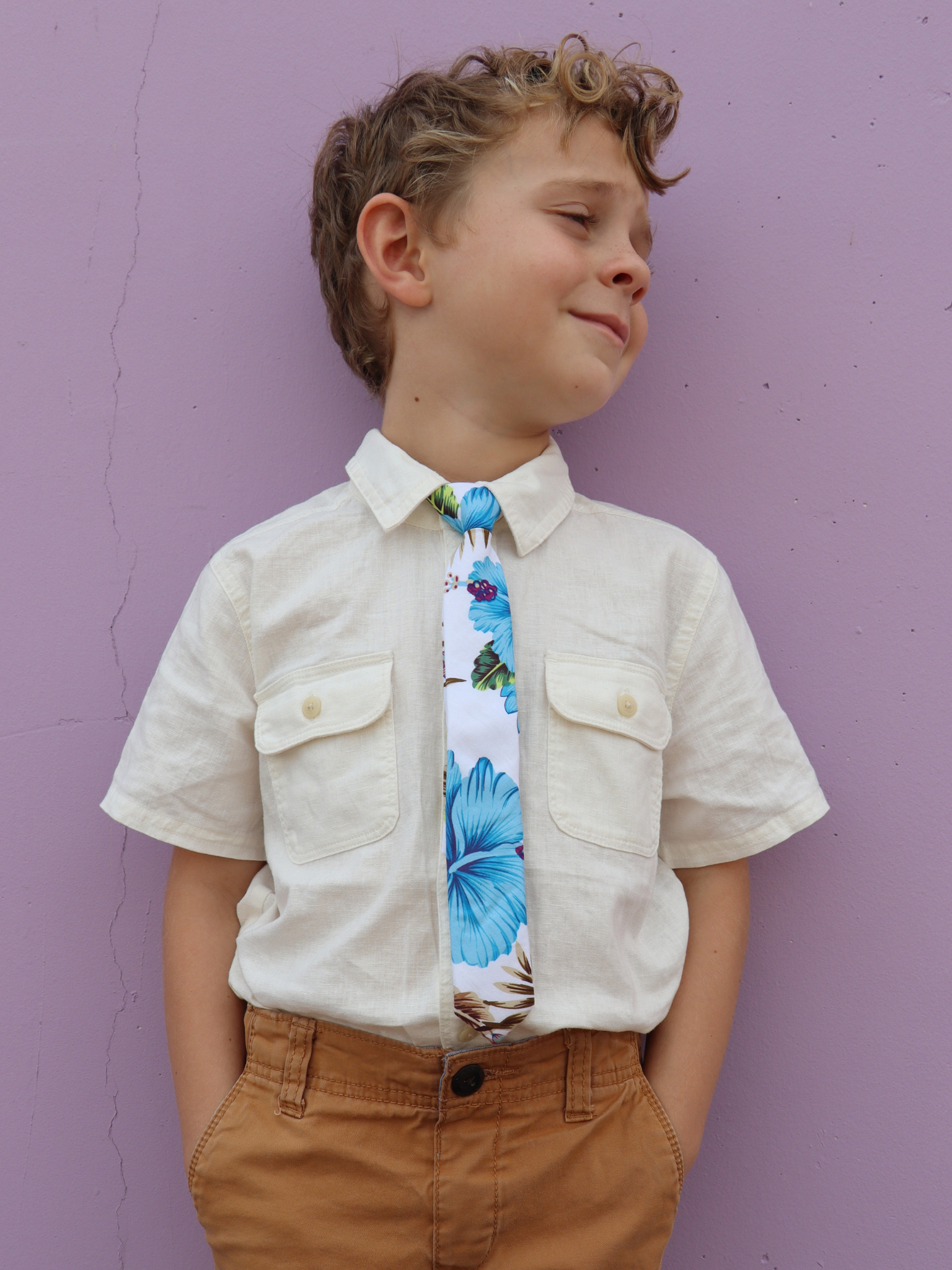 A boy in a white shirt with a white and blue floral pre tied tie for kids ages 1-12 available in 4 childrens sizes.