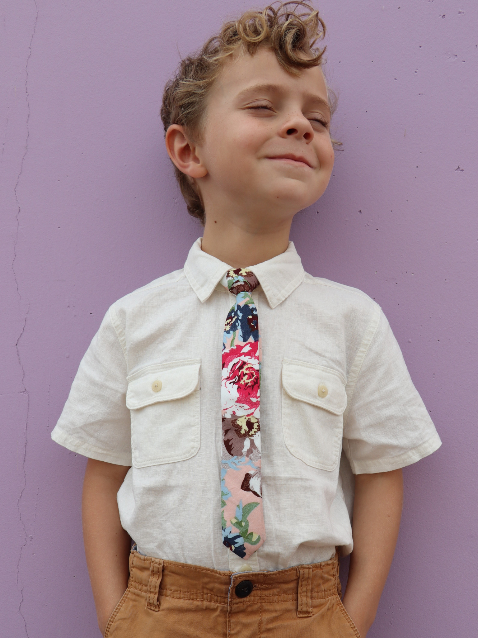 A boy in a white shirt with a pink, green, and blue floral pre tied tie for kids ages 1-12 available in 4 childrens sizes.