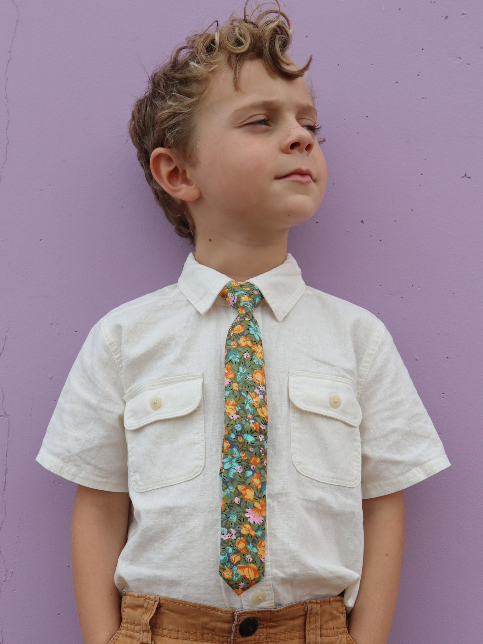 A boy in a white shirt with a green, gray, and orange floral pre tied tie for kids ages 1-12 available in 4 childrens sizes.