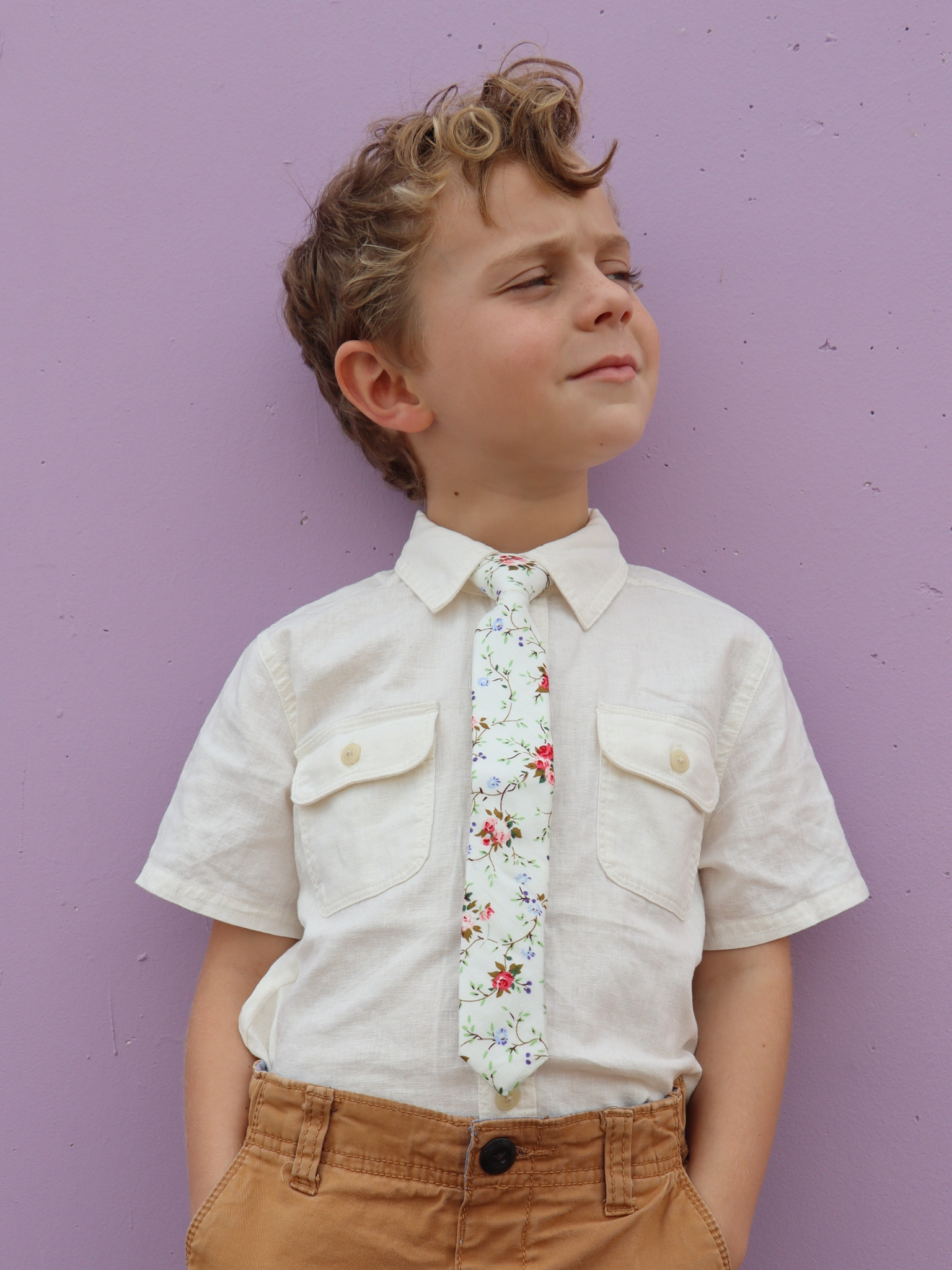 A boy in a white shirt with a white, pink, and blue floral pre tied tie for kids ages 1-12 available in 4 childrens sizes.