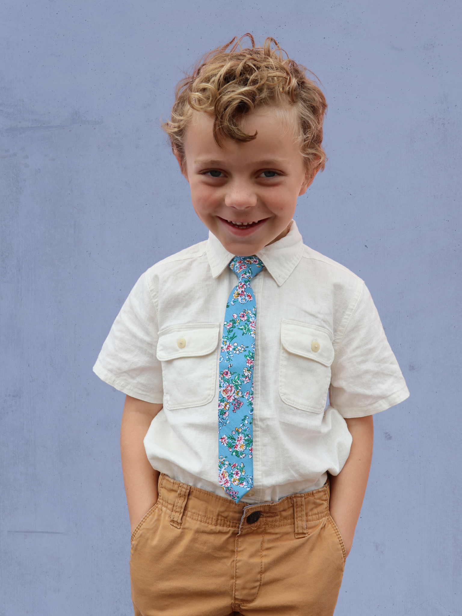 A boy in a white shirt with a blue and purple floral pre tied tie for kids ages 1-12 available in 4 childrens sizes.