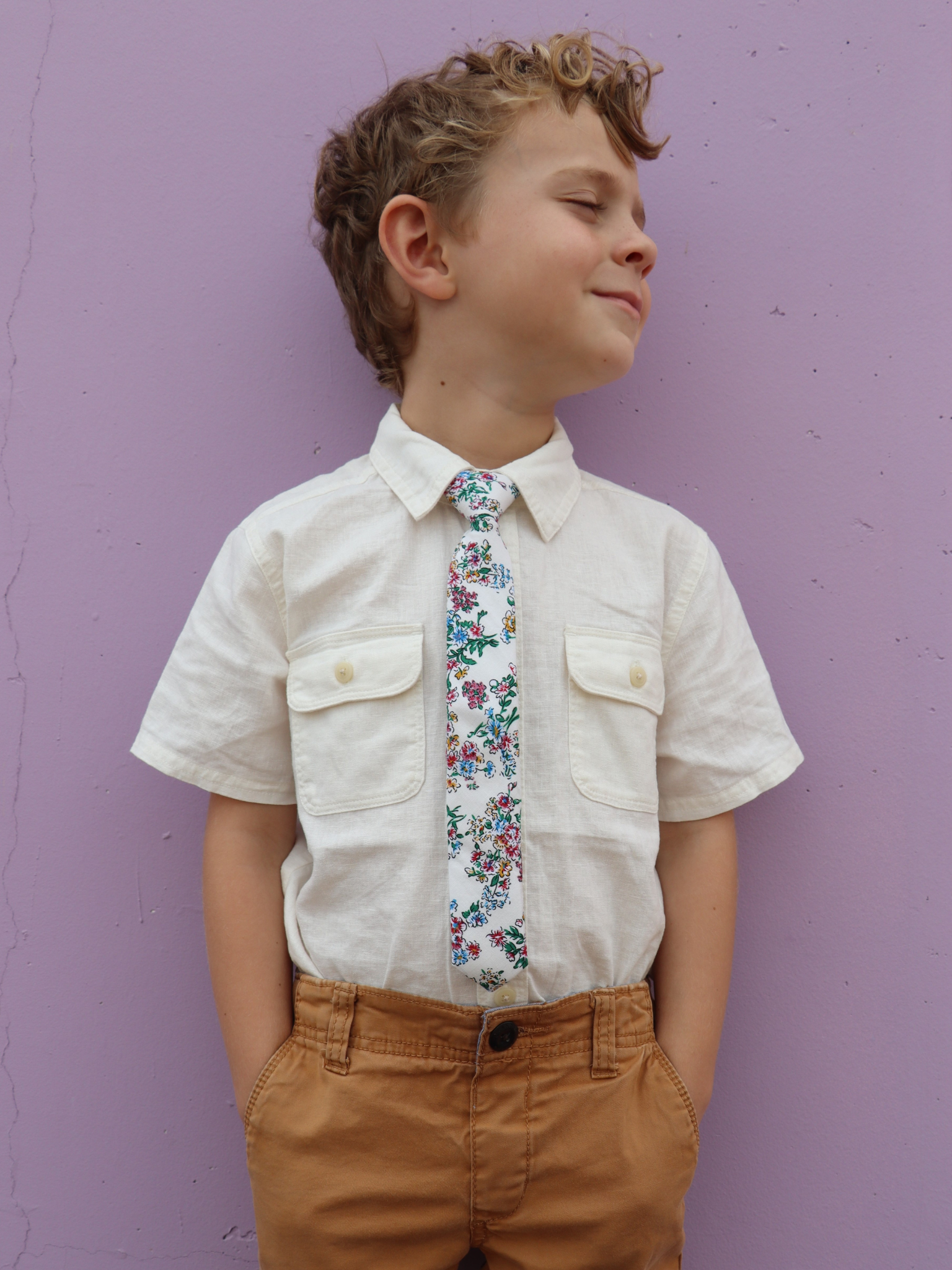 A boy in a white shirt with a red, white and blue floral pre tied tie for kids ages 1-12 available in 4 childrens sizes.