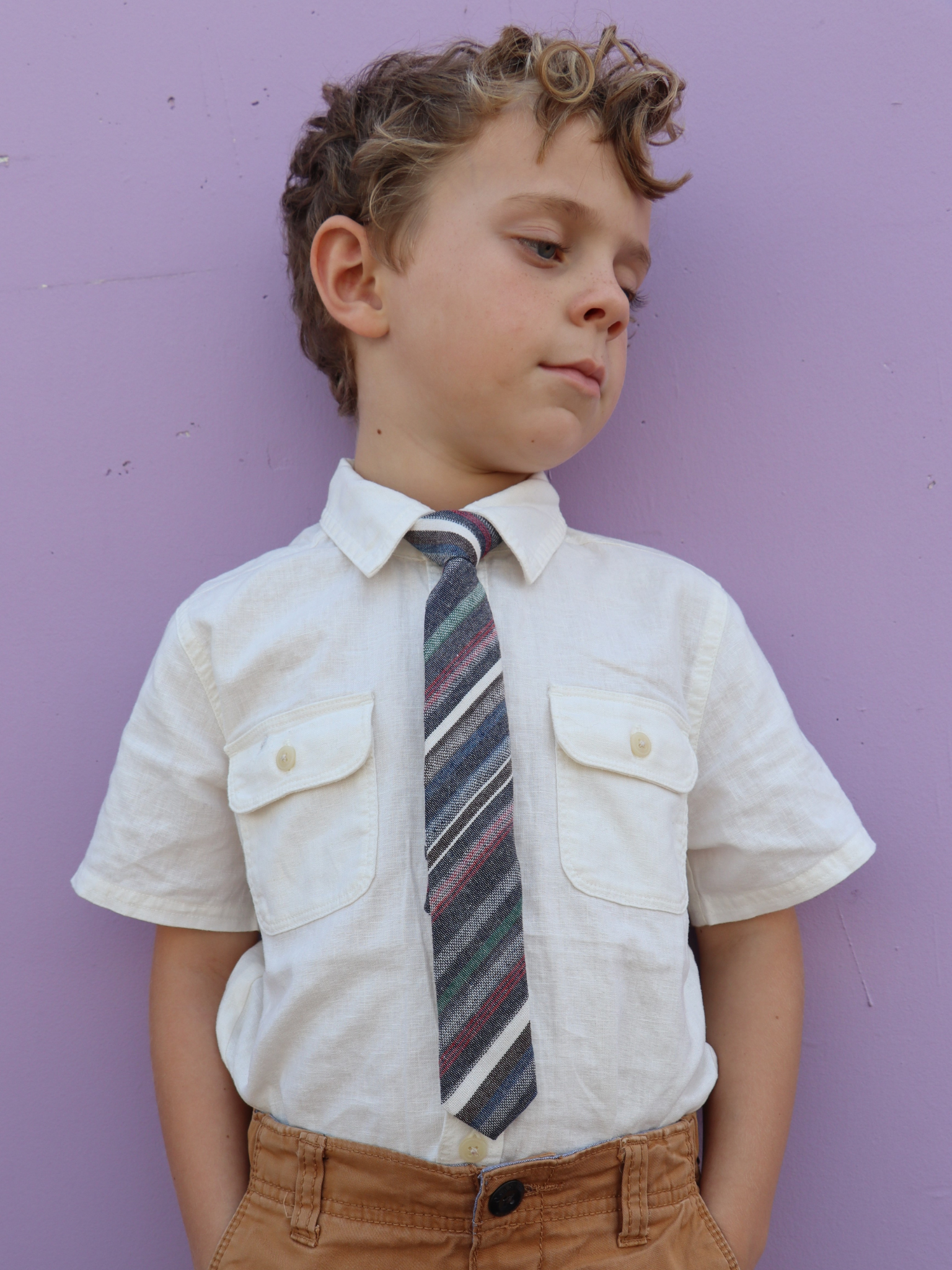 A boy in a white shirt with a gray, green, and red striped pre tied tie for kids ages 1-12 available in 4 childrens sizes.