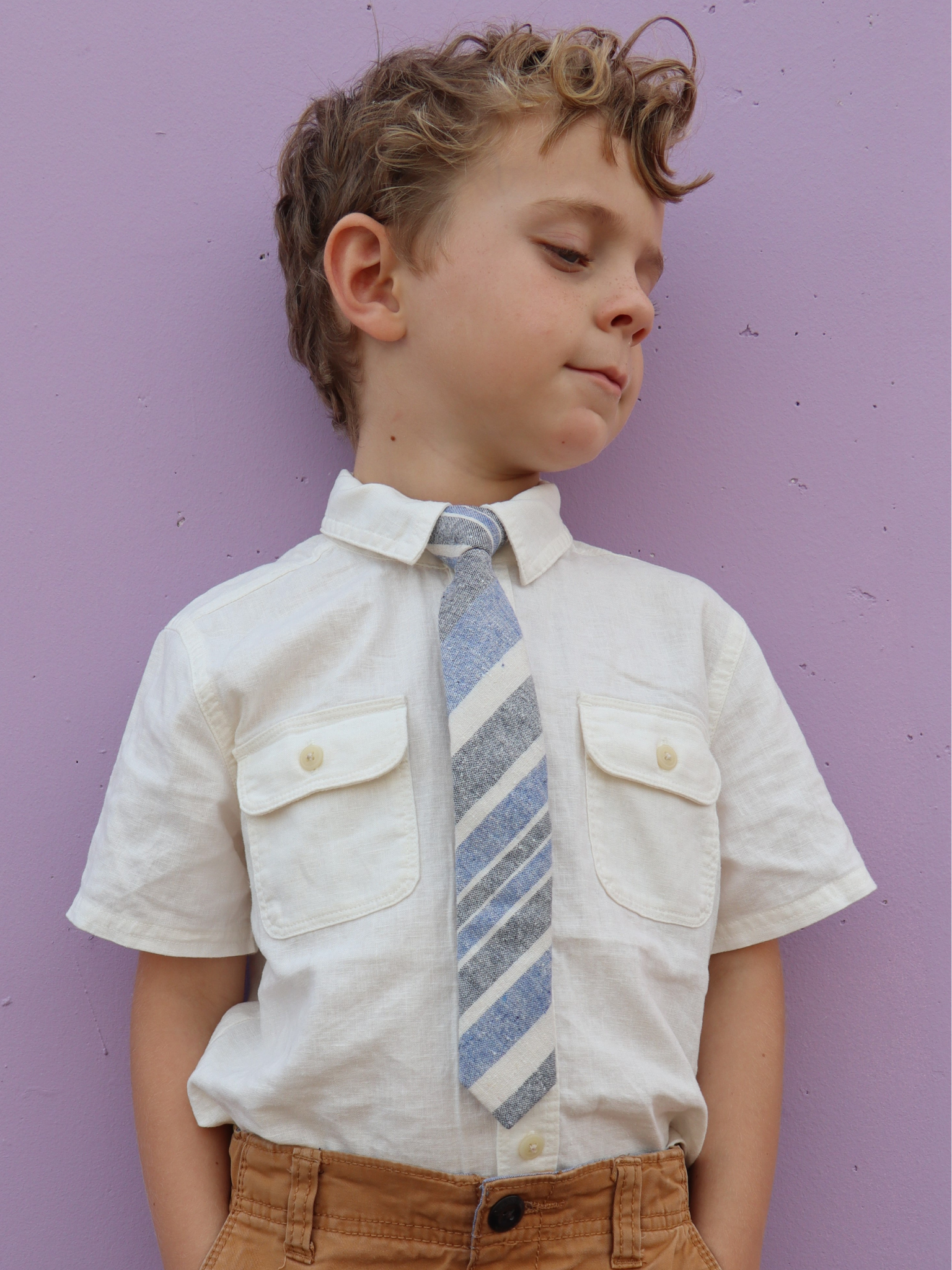 A boy in a white shirt with a blue, beige, and gray striped pre tied tie for kids ages 1-12 available in 4 childrens sizes.