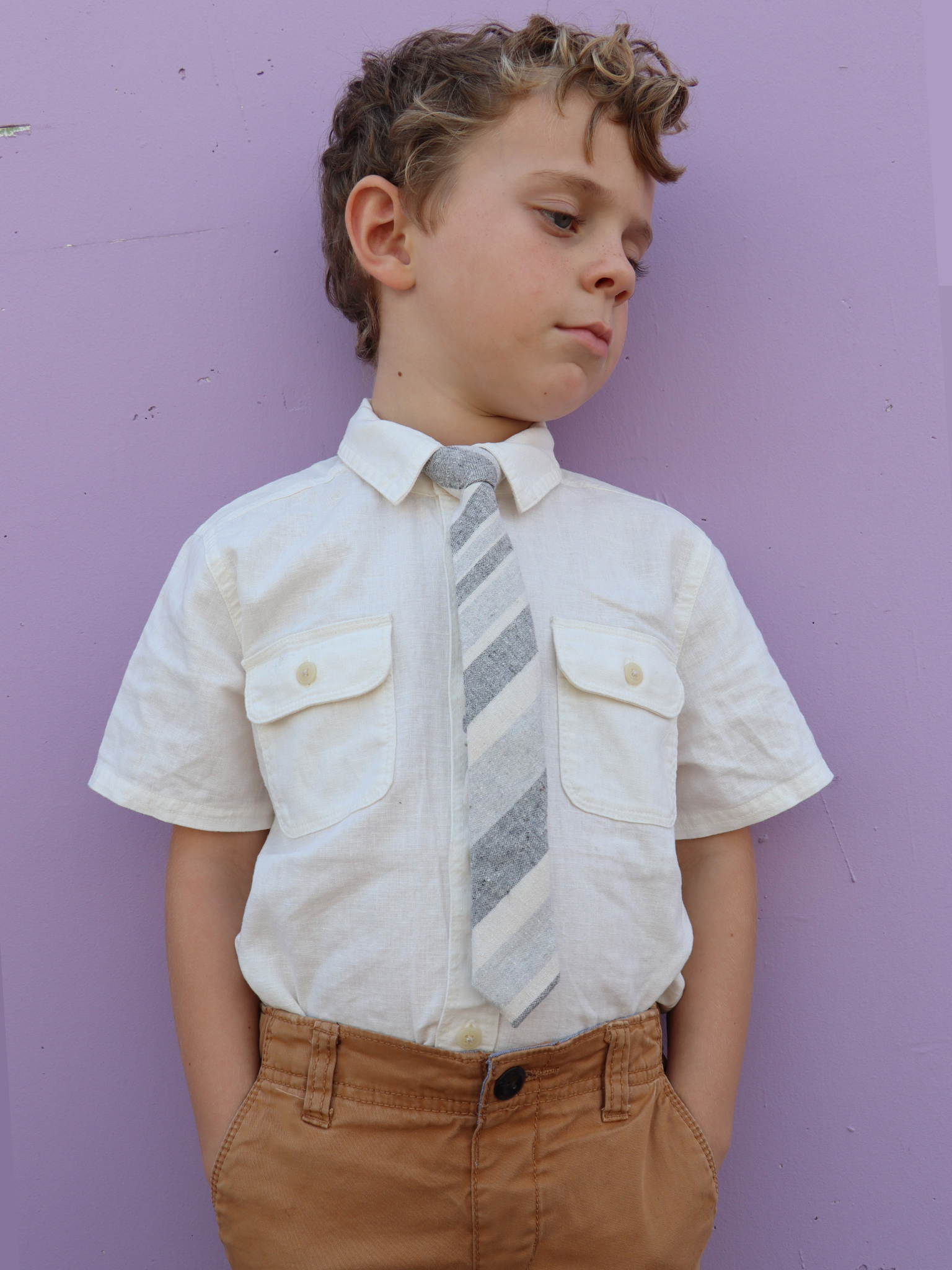 A boy in a white shirt with a grey and cream striped pre tied tie for kids ages 1-12 available in 4 childrens sizes.