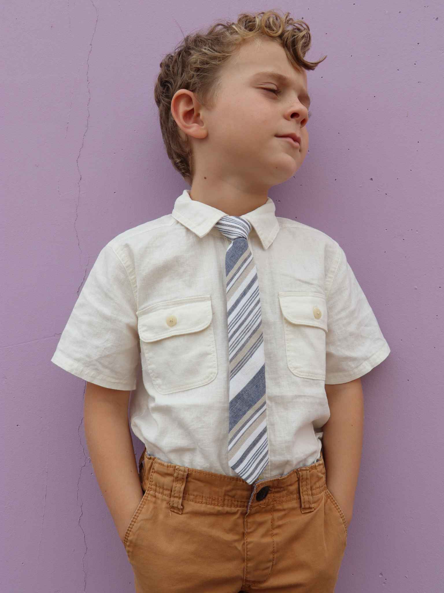 A boy in a white shirt with a blue, white, and gold striped pre tied tie for kids ages 1-12 available in 4 childrens sizes.