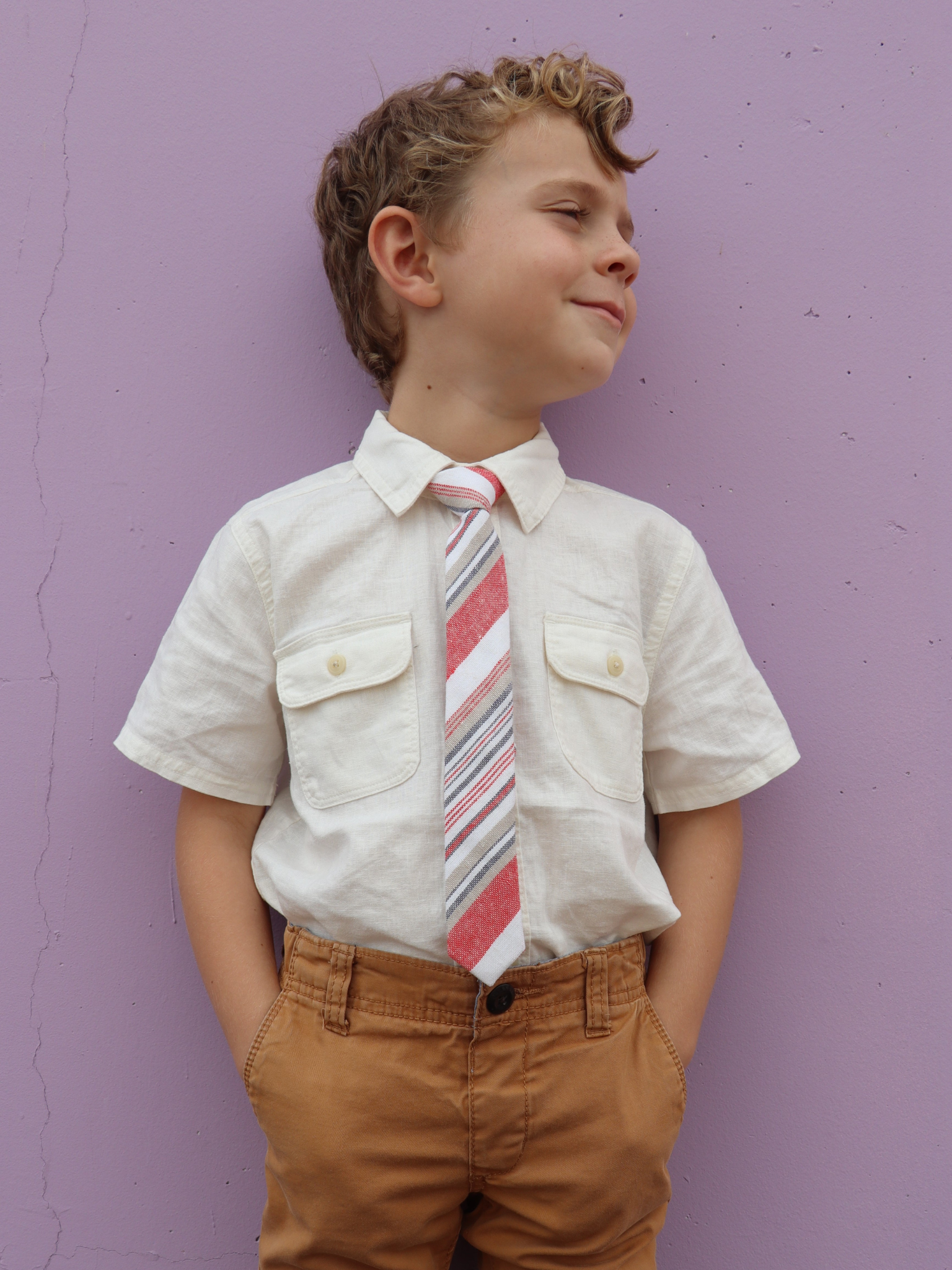 A boy in a white shirt with a red, white, and gold striped pre tied tie for kids ages 1-12 available in 4 childrens sizes.