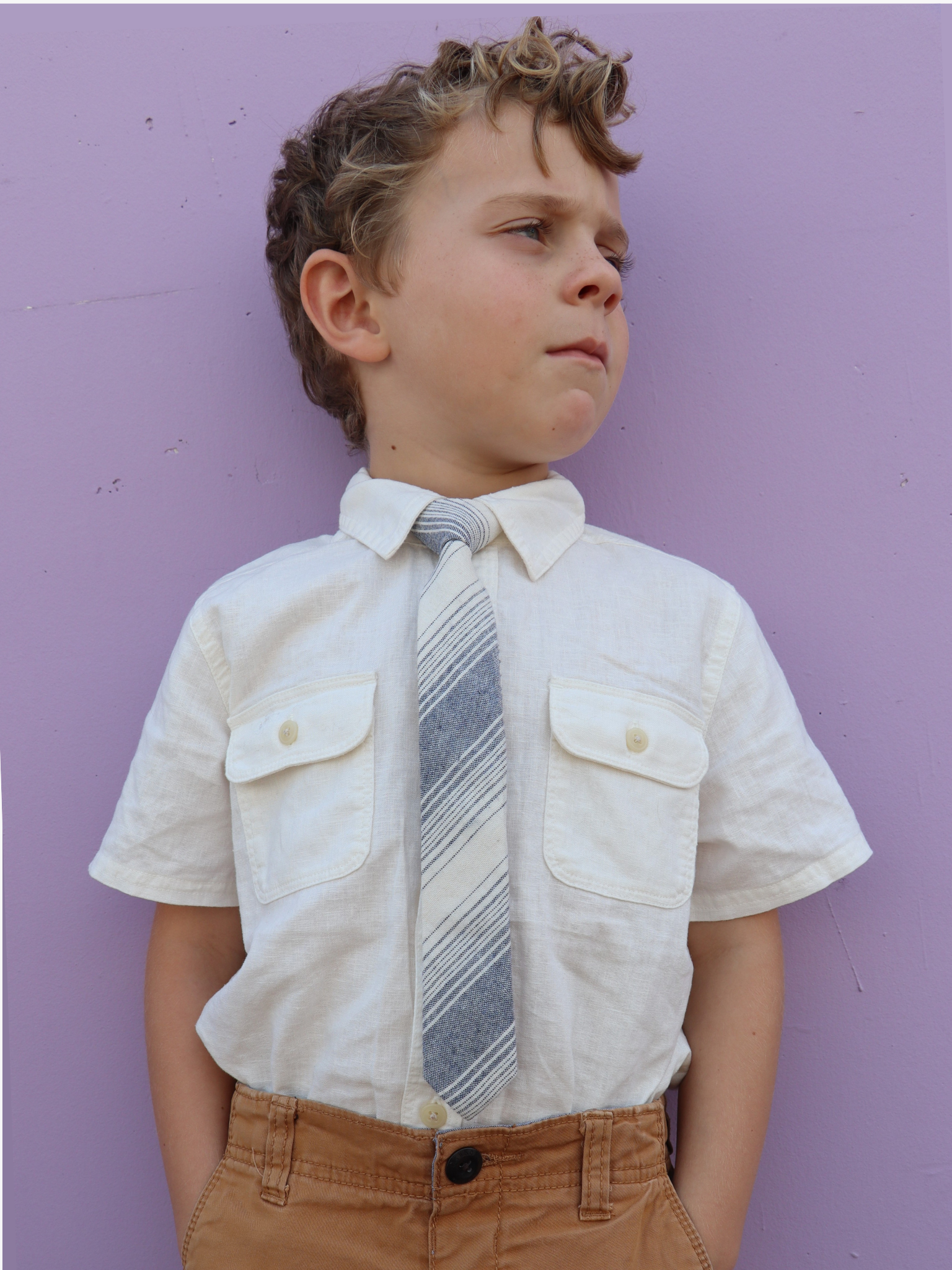 A boy in a white shirt with a navy blue and beigestriped pre tied tie for kids ages 1-12 available in 4 childrens sizes.