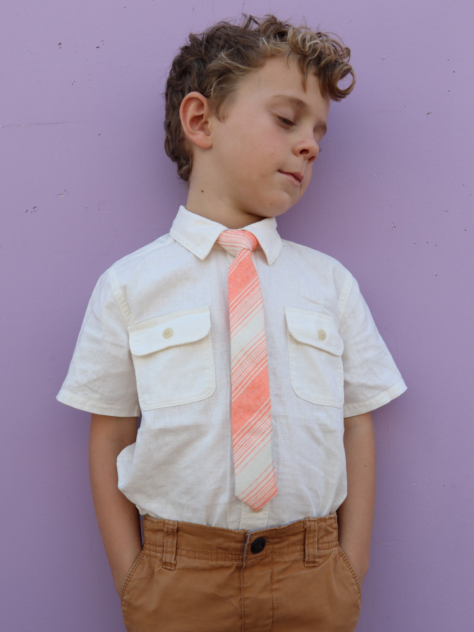 A boy in a white shirt with an orange and cream striped pre tied tie for kids ages 1-12 available in 4 childrens sizes.