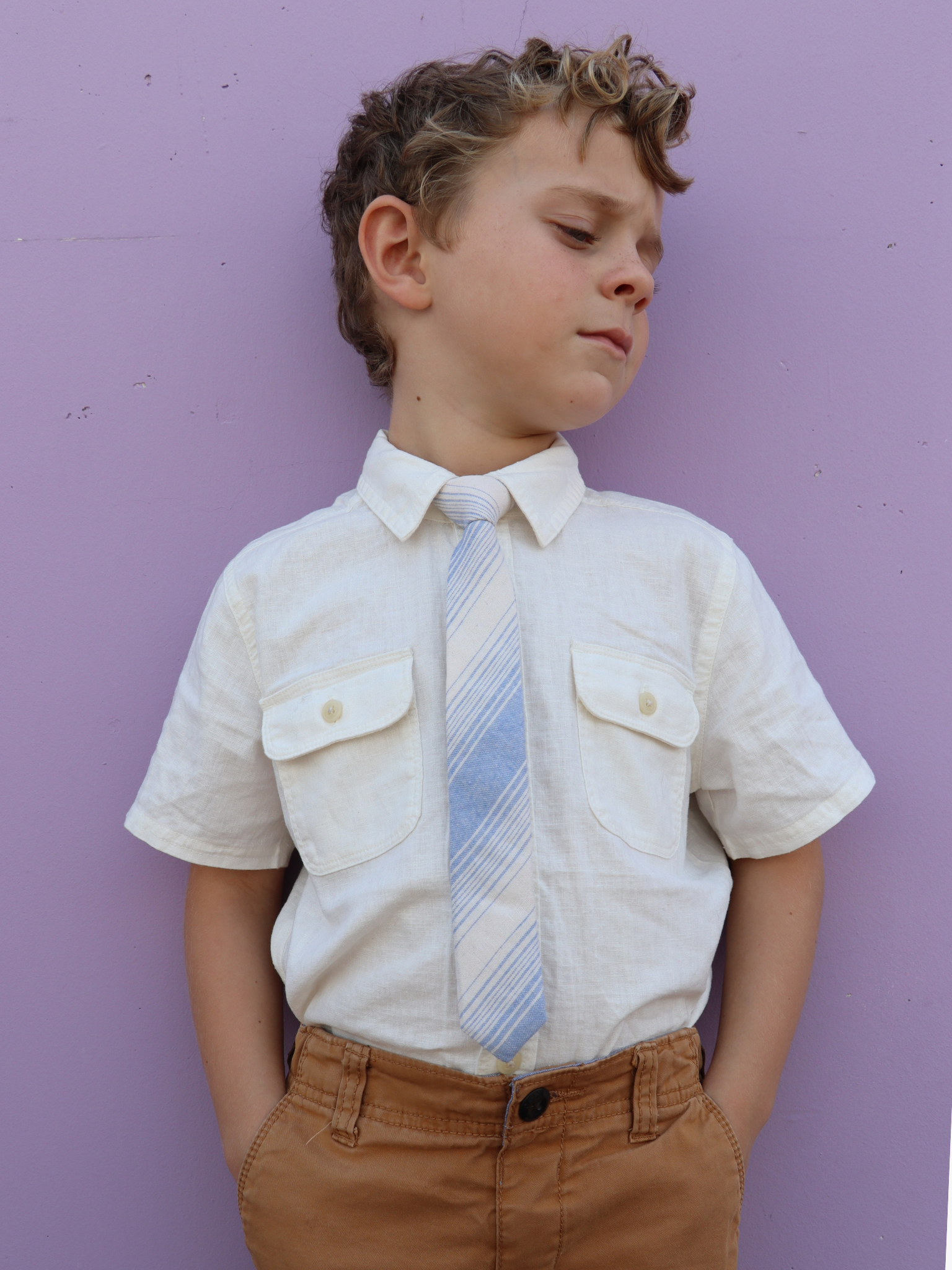 A boy in a white shirt with a light blue and beige striped pre tied tie for kids ages 1-12 available in 4 childrens sizes.