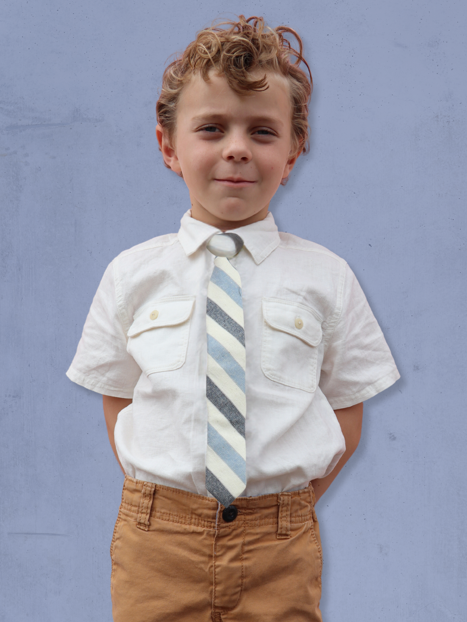 A boy in a white shirt with a blue, white, and navy striped pre tied tie for kids ages 1-12 available in 4 childrens sizes.