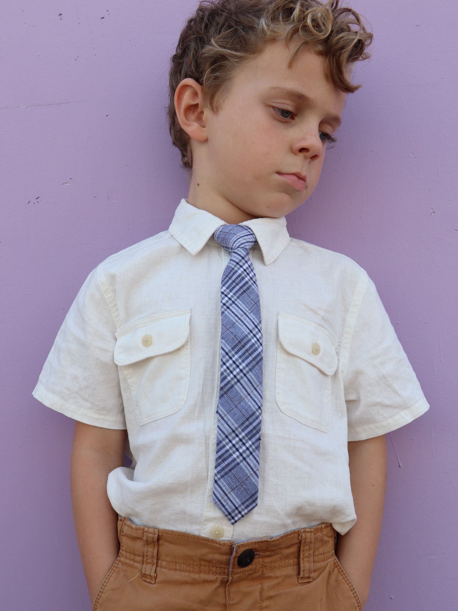 A boy in a white shirt with a blue and white plaid pre tied tie for kids ages 1-12 available in 4 childrens sizes.