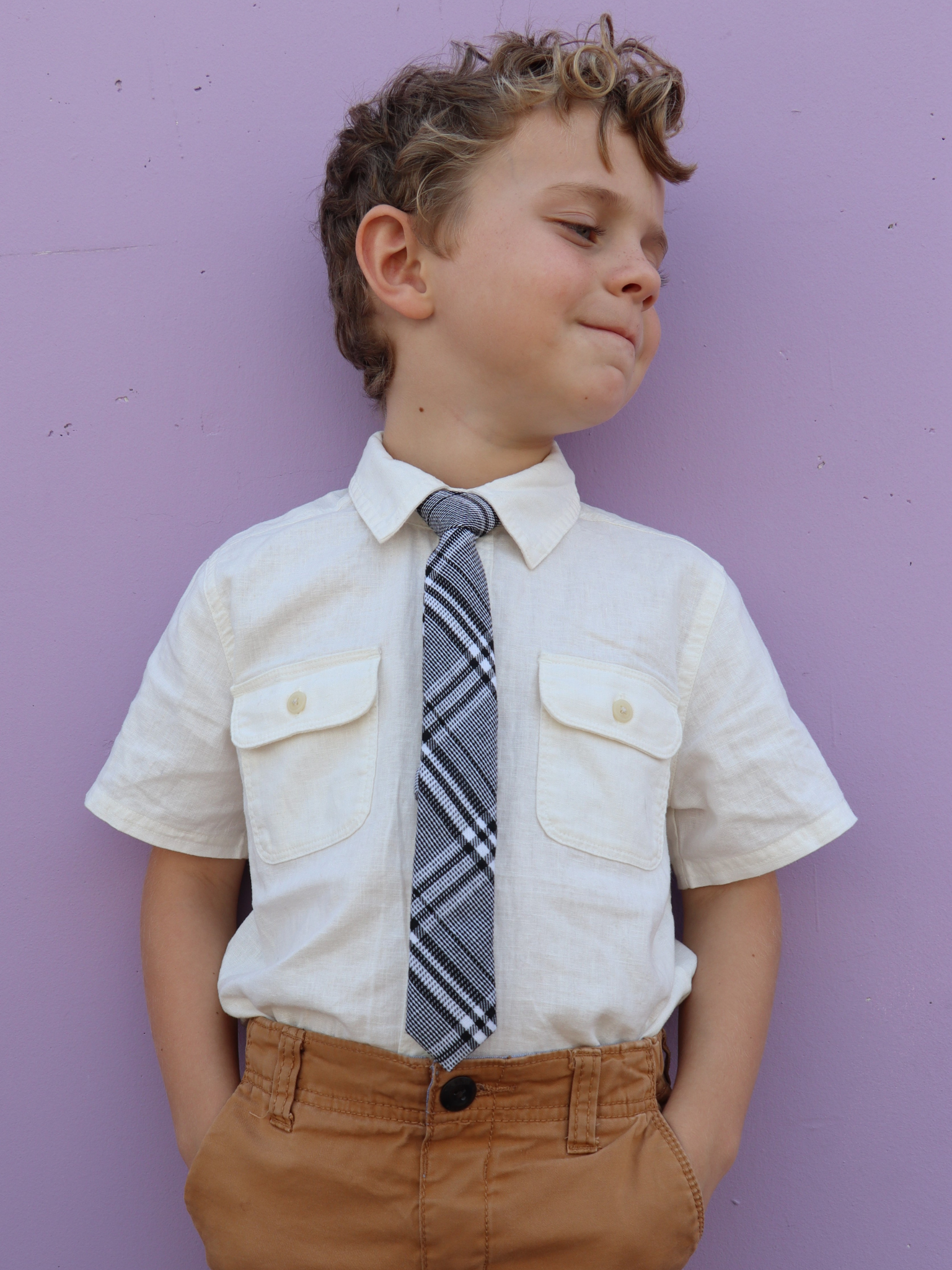 A boy in a white shirt with a black and white plaid pre tied tie for kids ages 1-12 available in 4 childrens sizes.