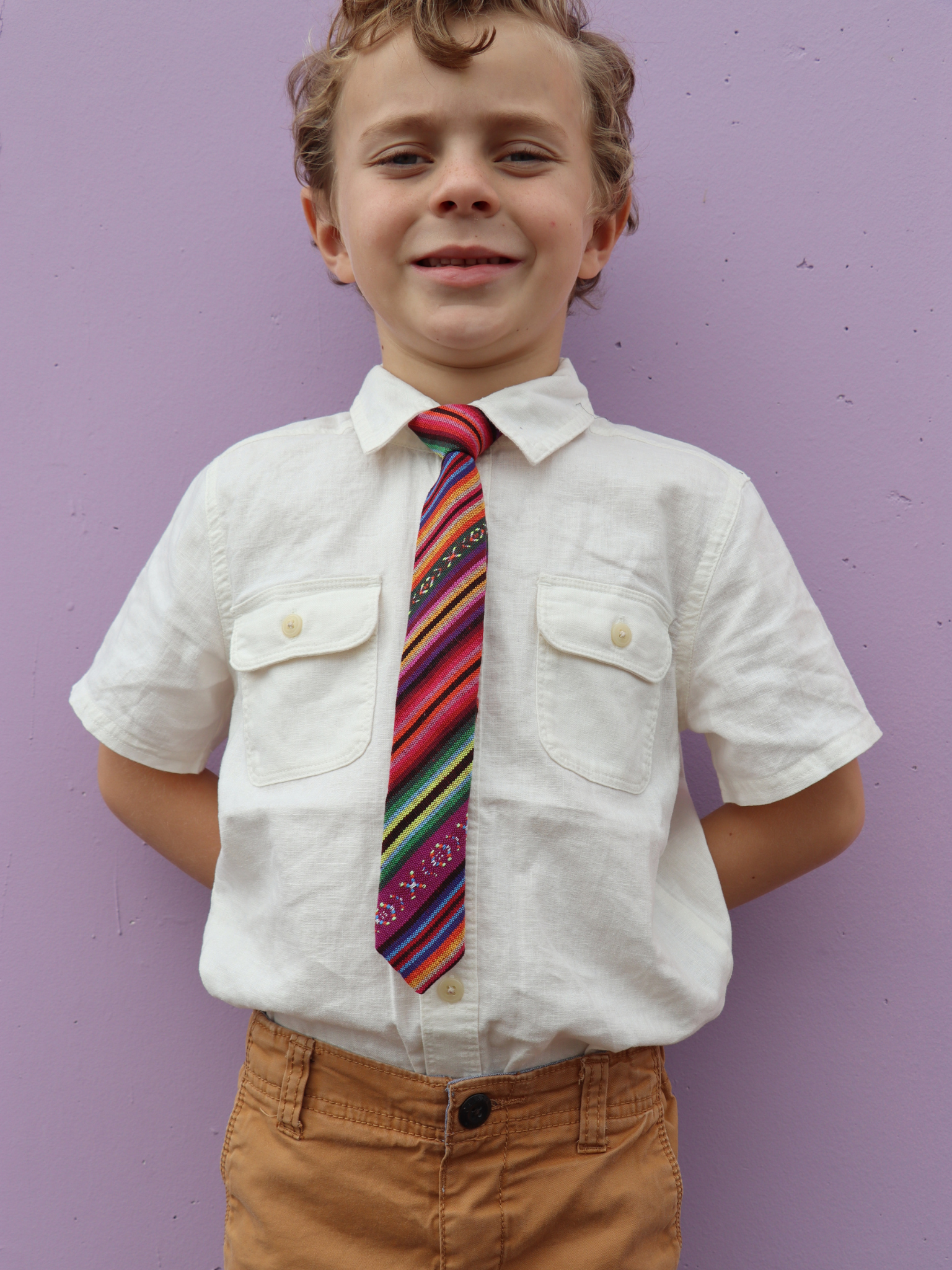 A boy in a white shirt with a purple and green striped pre tied tie for kids ages 1-12 available in 4 childrens sizes.