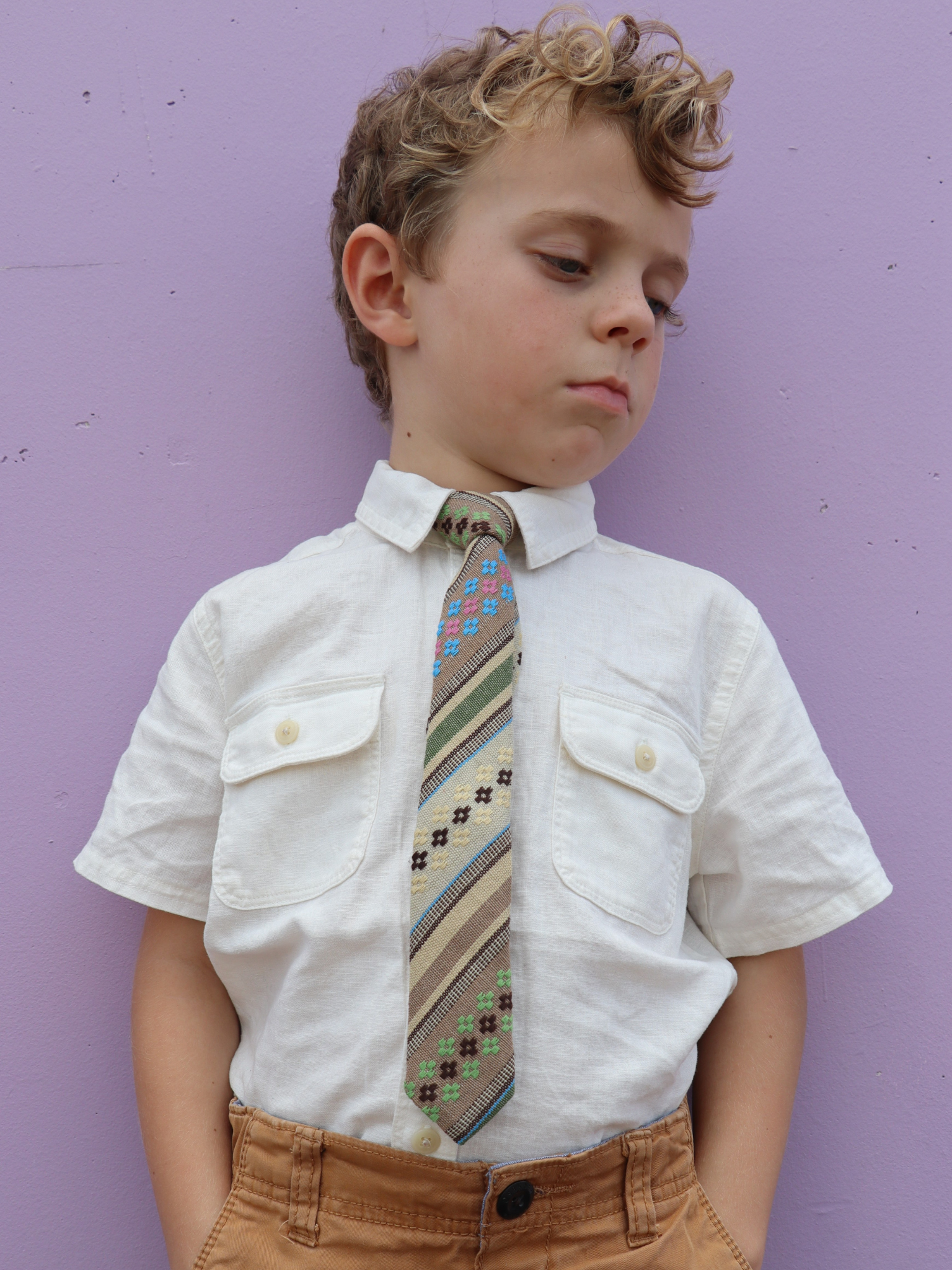 A boy in a white shirt with a green, tan, and brown striped pre tied tie for kids ages 1-12 available in 4 childrens sizes.