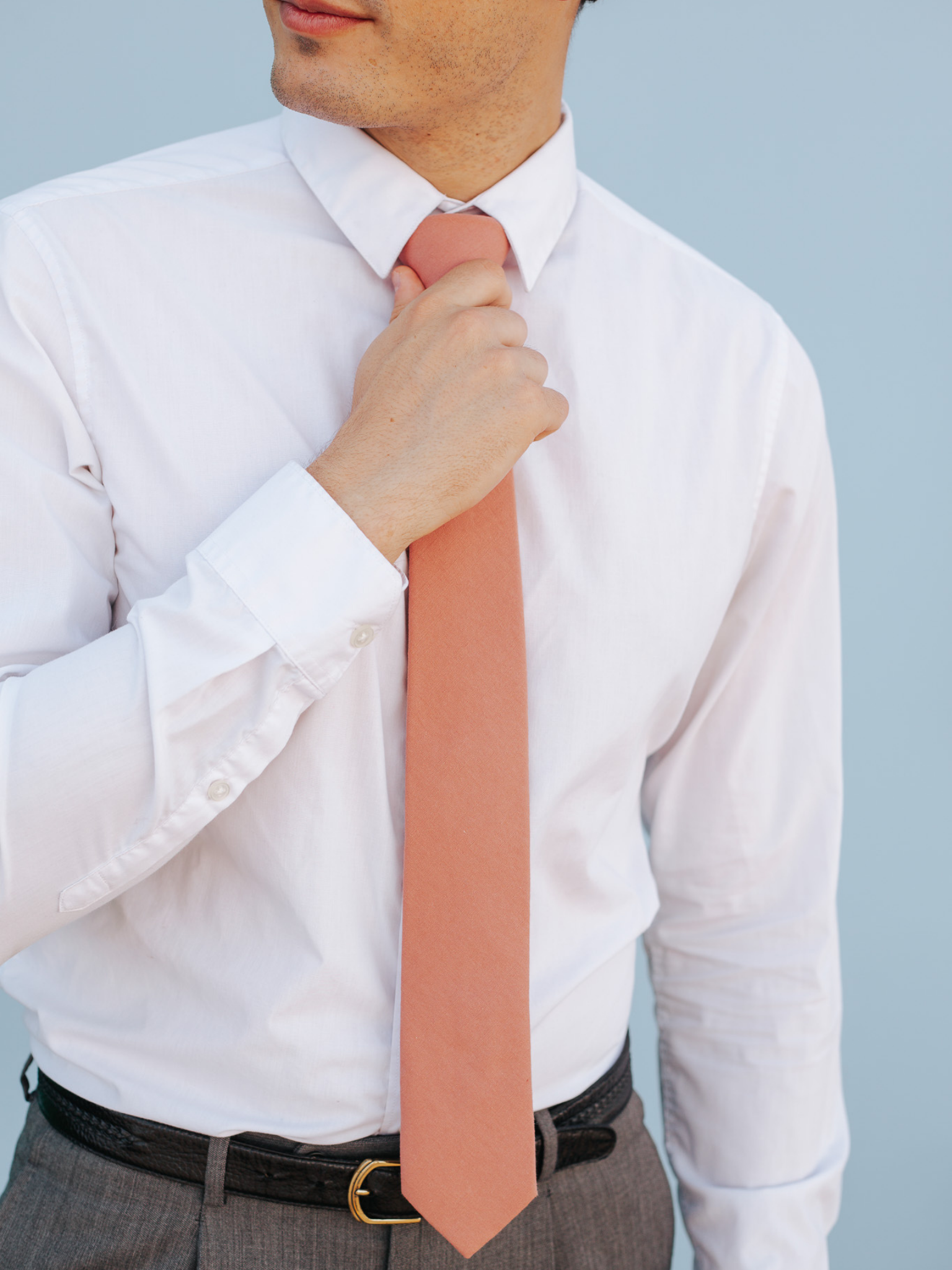 A close up of a man wearing a rosewood light pink solid-colored cotton skinny tie for weddings, grooms, and groomsmen.