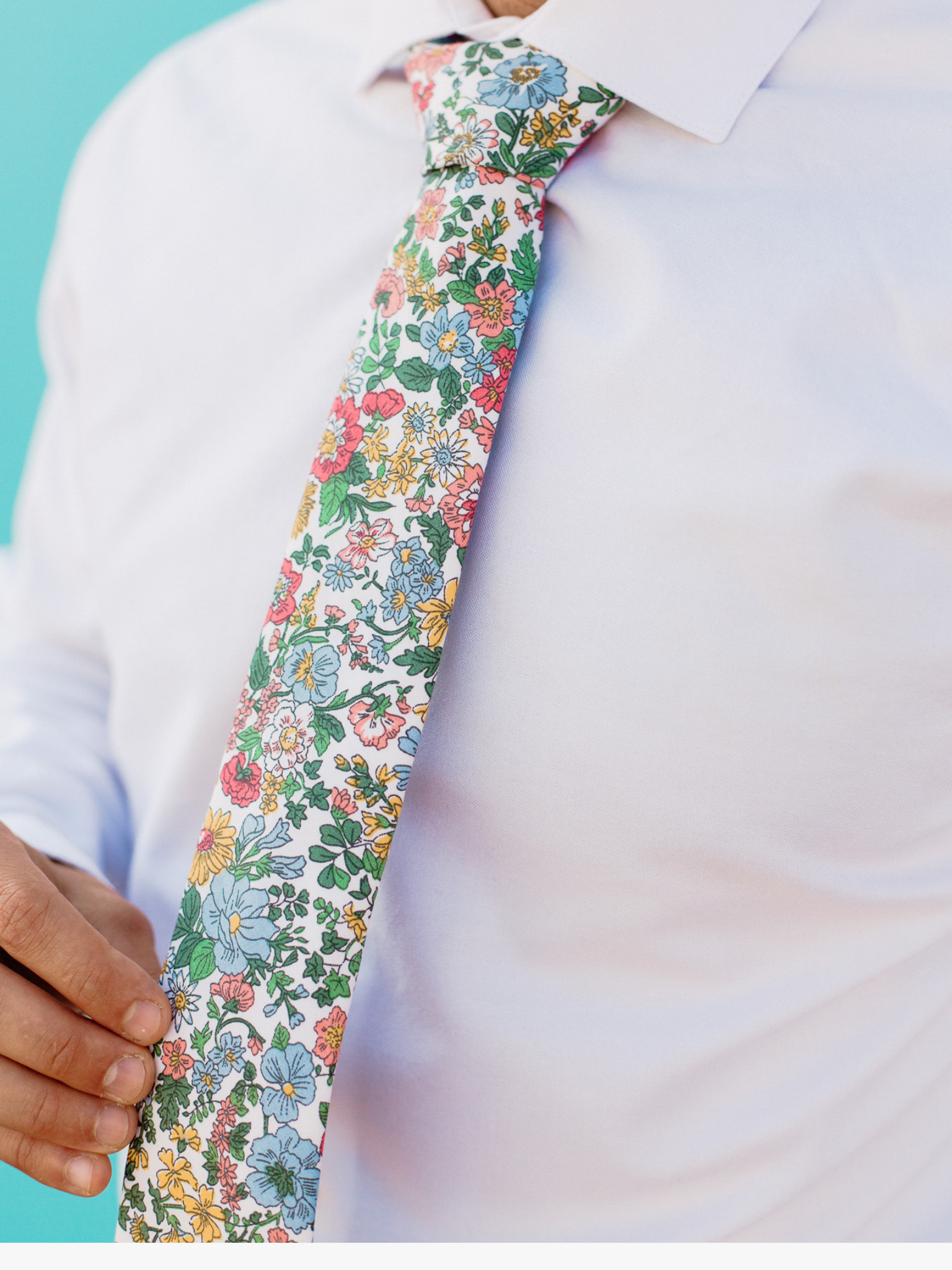 A close up of a man wearing a blue, pink, and green flower cotton skinny tie for weddings, grooms, and groomsmen.