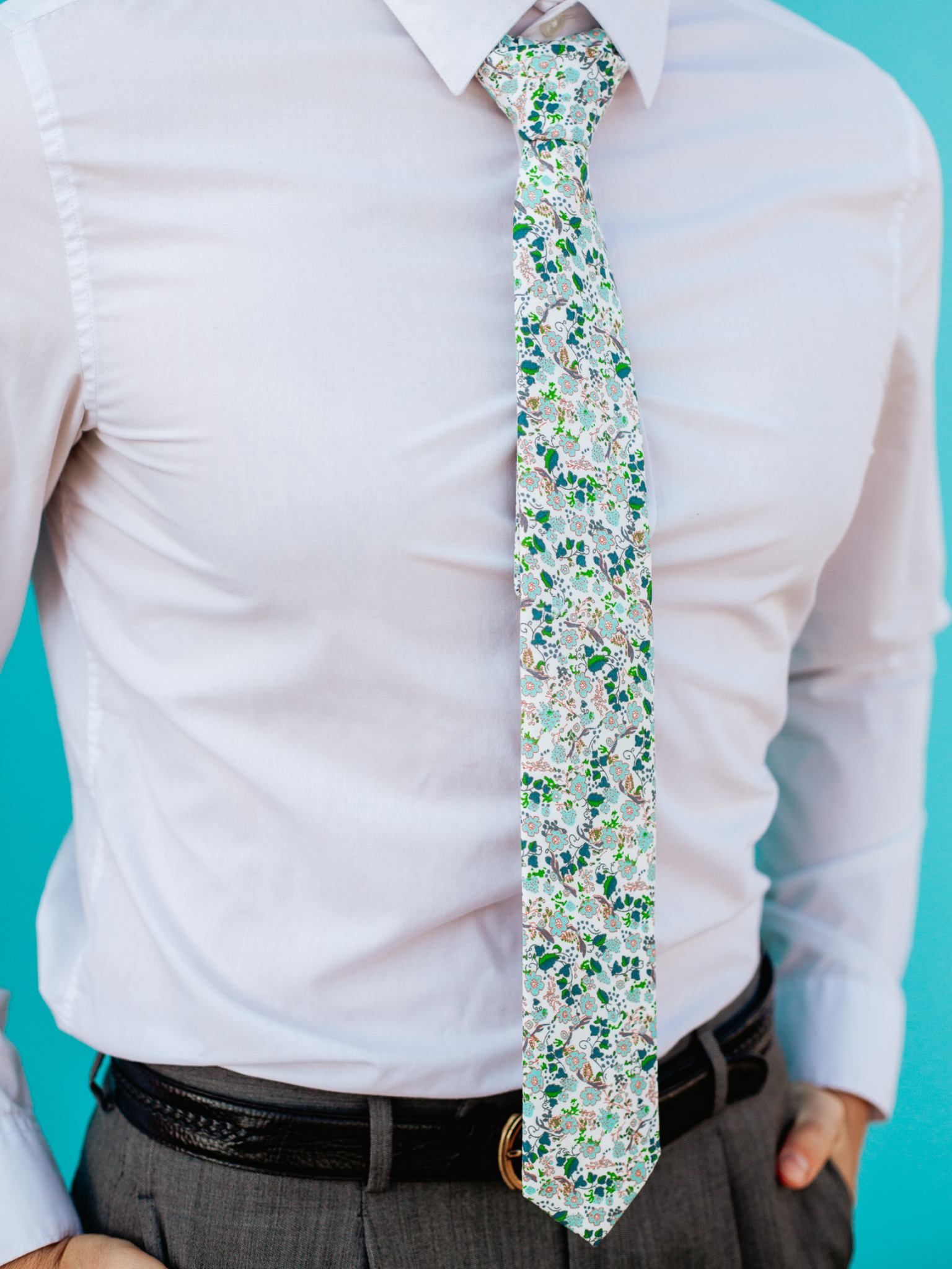 A close up of a man wearing a white and light blue flower cotton skinny tie for weddings, grooms, and groomsmen.