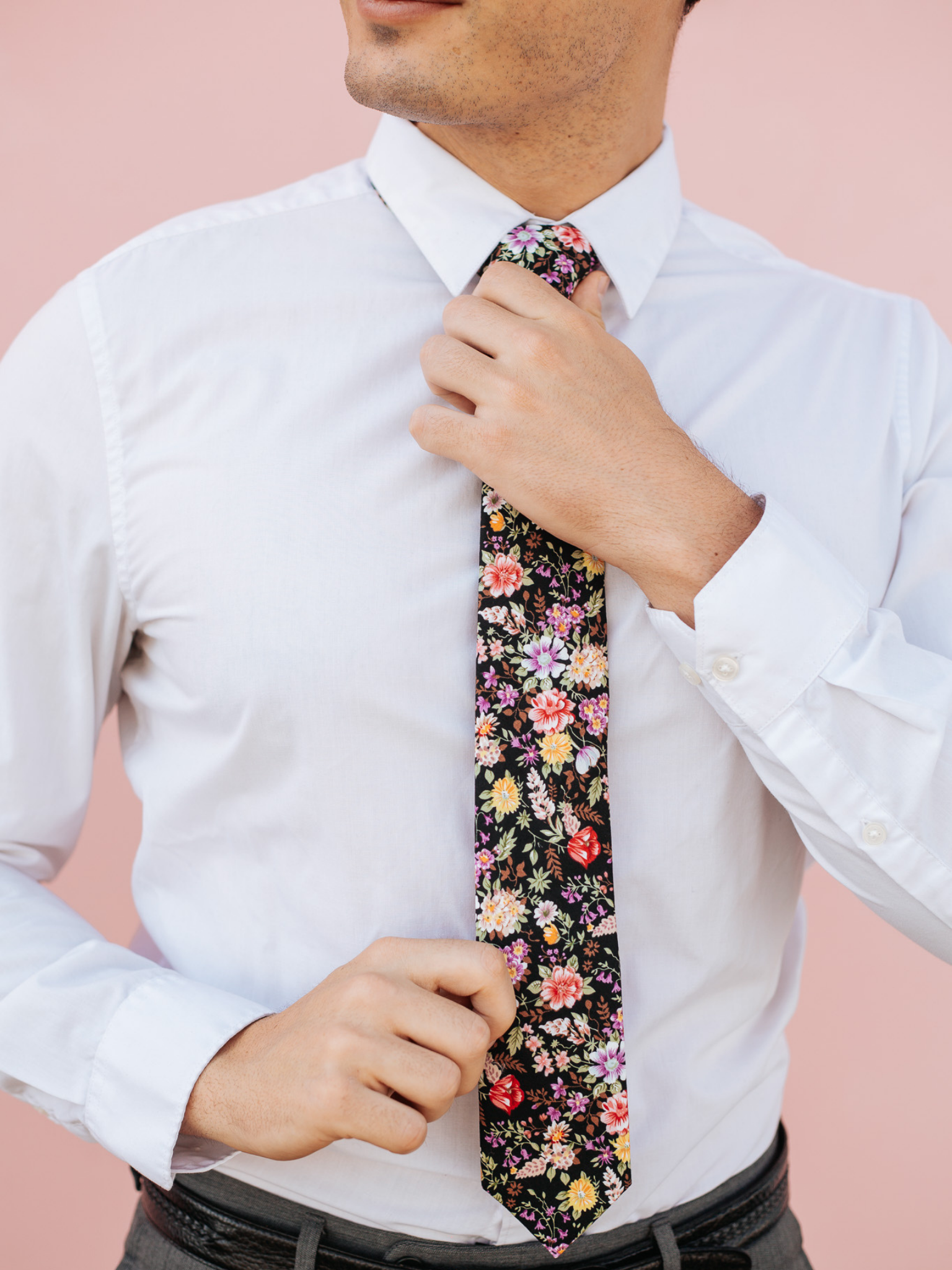 A close up of a man wearing a black, brown, and pink flower cotton skinny tie for weddings, grooms, and groomsmen.