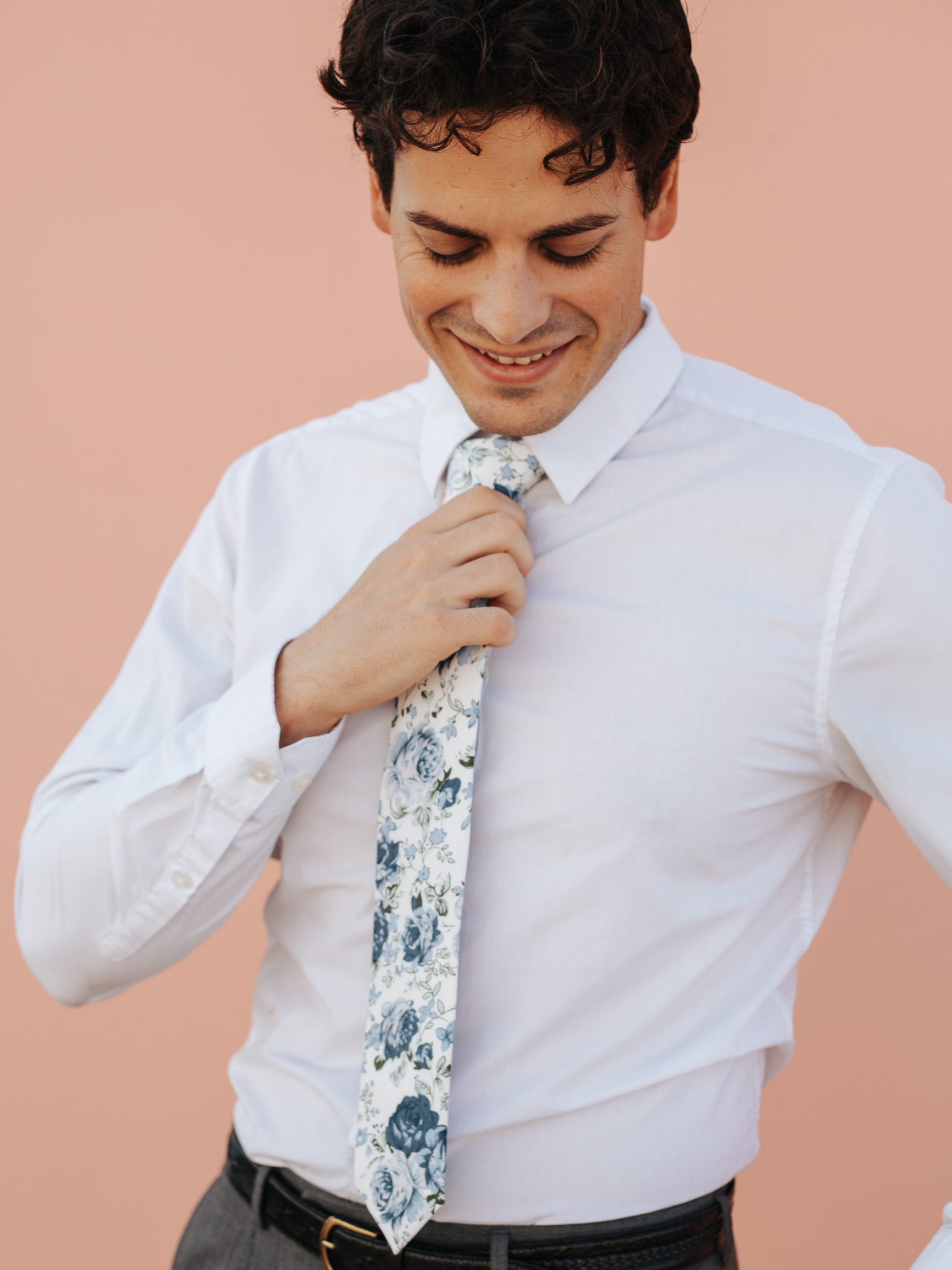 A close up of a man wearing a off-white and blue flower cotton skinny tie for weddings, grooms, and groomsmen.