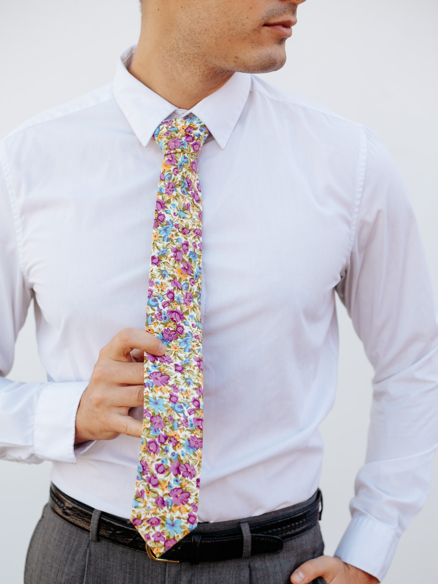 A close up of a man wearing a purple, green and blue flower cotton skinny tie for weddings, grooms, and groomsmen.