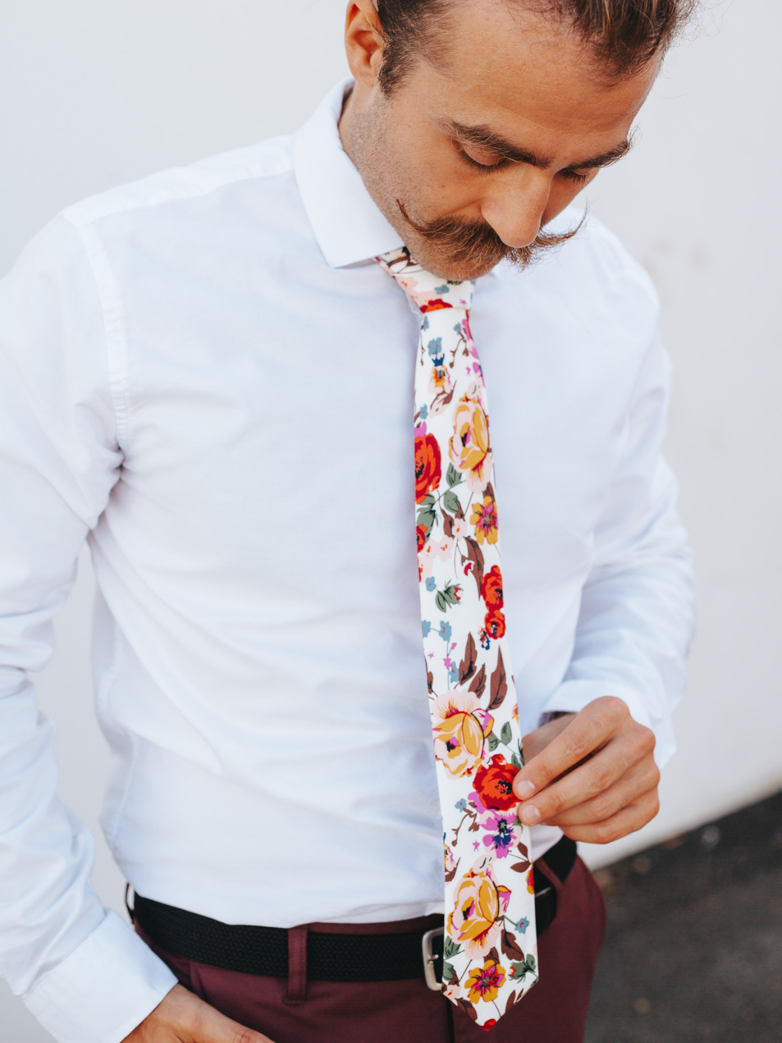 A close up of a man wearing a white and red/orange flower cotton skinny tie for weddings, grooms, and groomsmen.