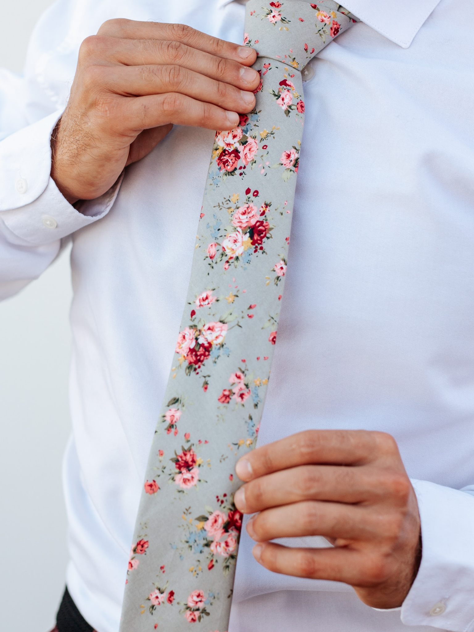 A close up of a man wearing a beige and red flower cotton skinny tie for weddings, grooms, and groomsmen.