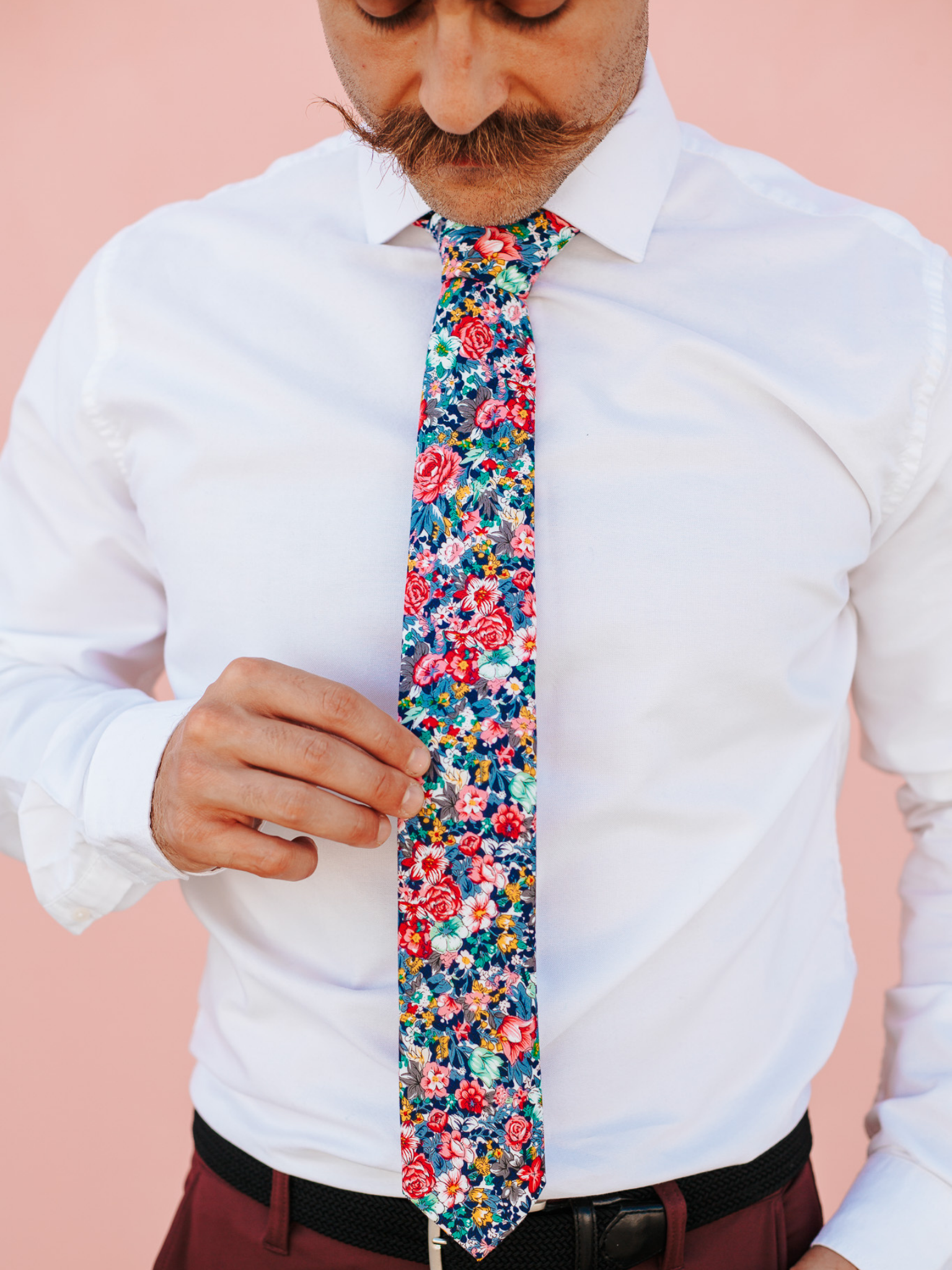 A close up of a man wearing a blue and pink flower cotton skinny tie for weddings, grooms, and groomsmen.