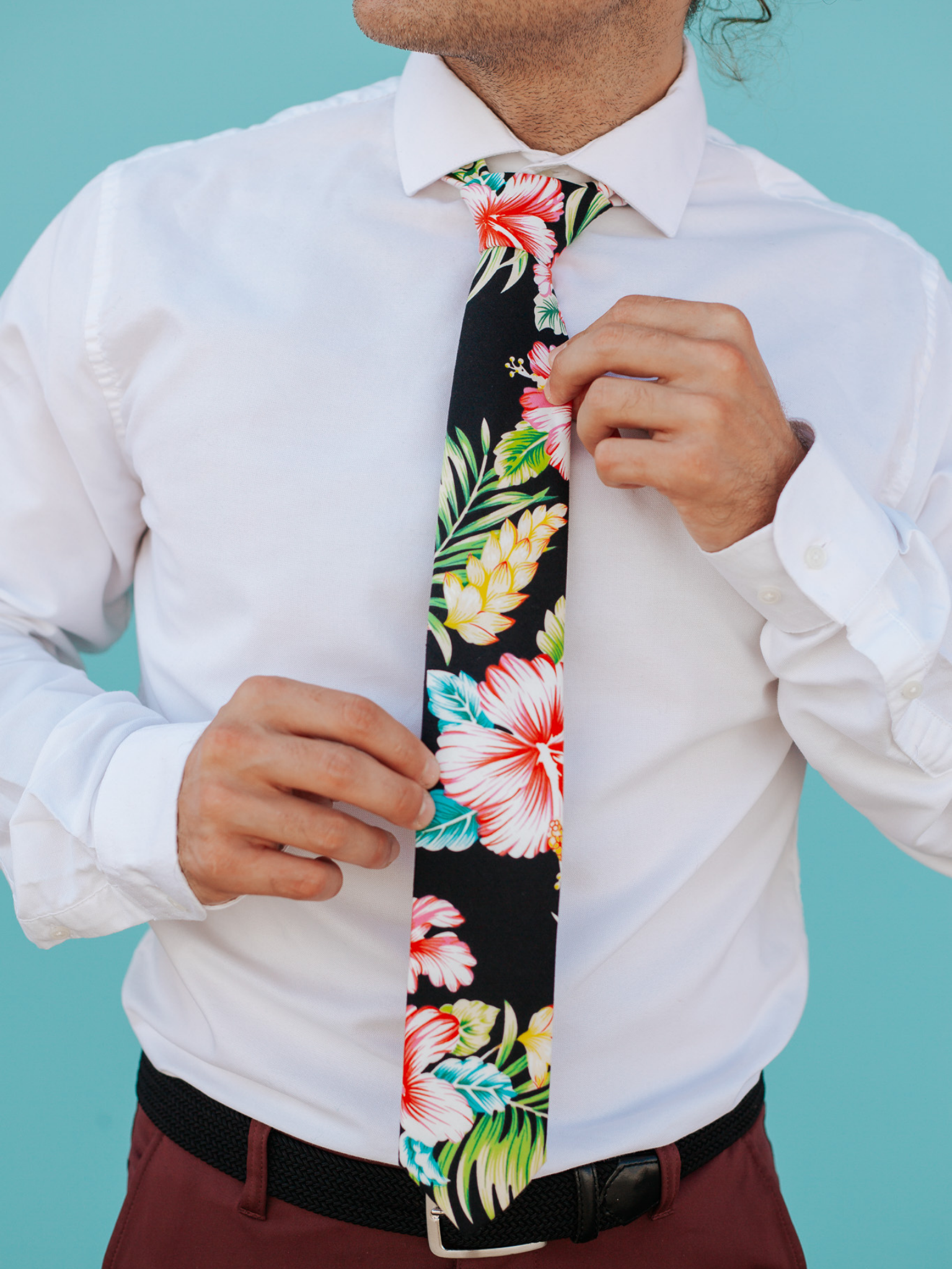 A close up of a man wearing a black, green, and pink flower cotton skinny tie for weddings, grooms, and groomsmen.