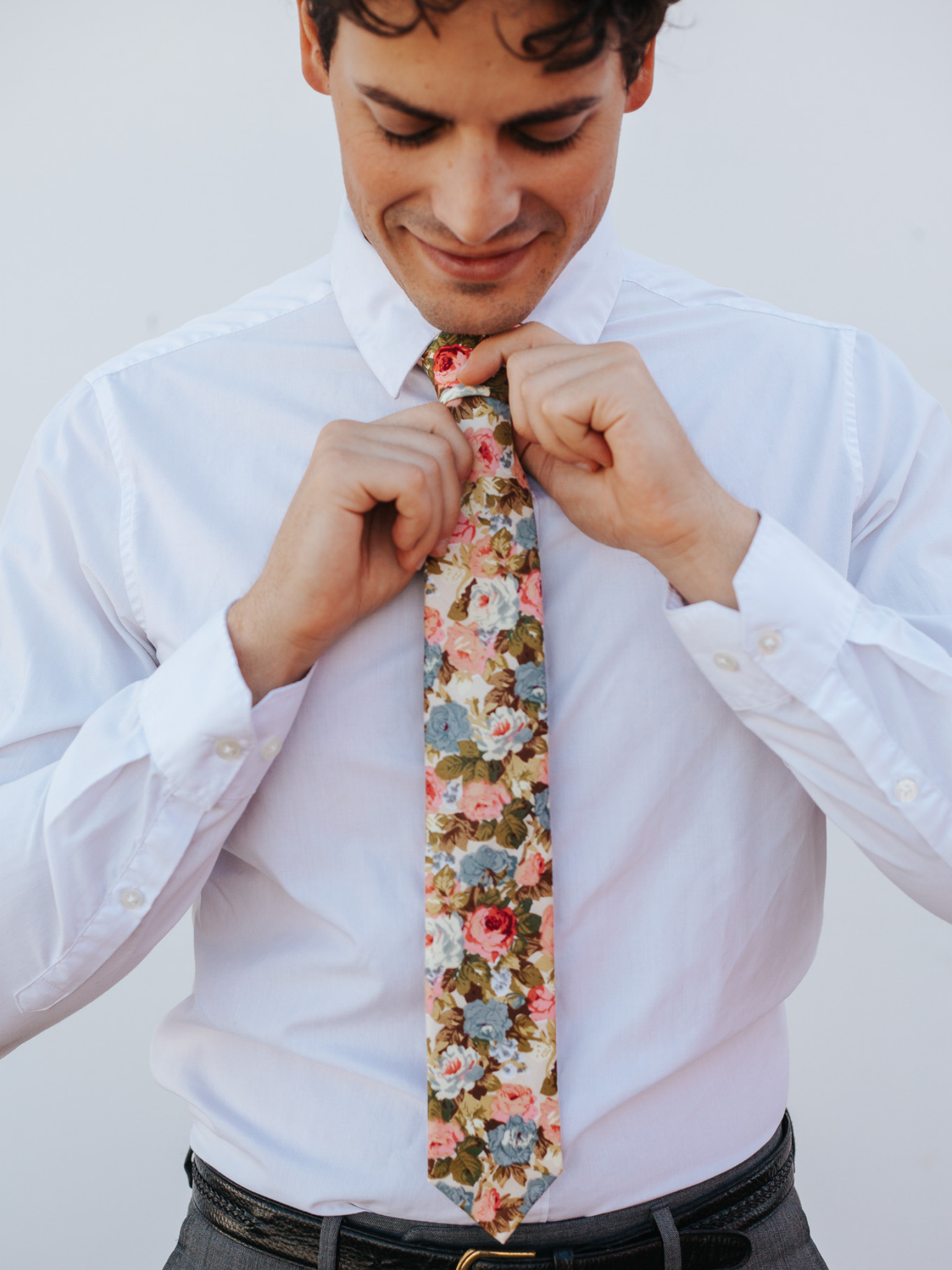 A close up of a man wearing a cream, blue, and pink flower cotton skinny tie for weddings, grooms, and groomsmen.