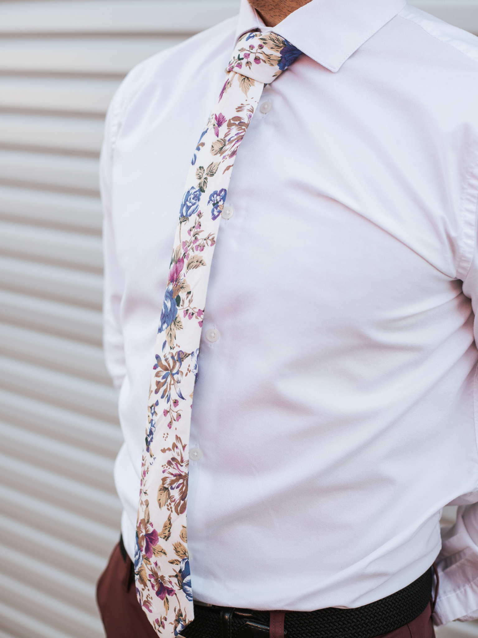 A close up of a man wearing a beige, blue, and purple flower cotton skinny tie for weddings, grooms, and groomsmen.